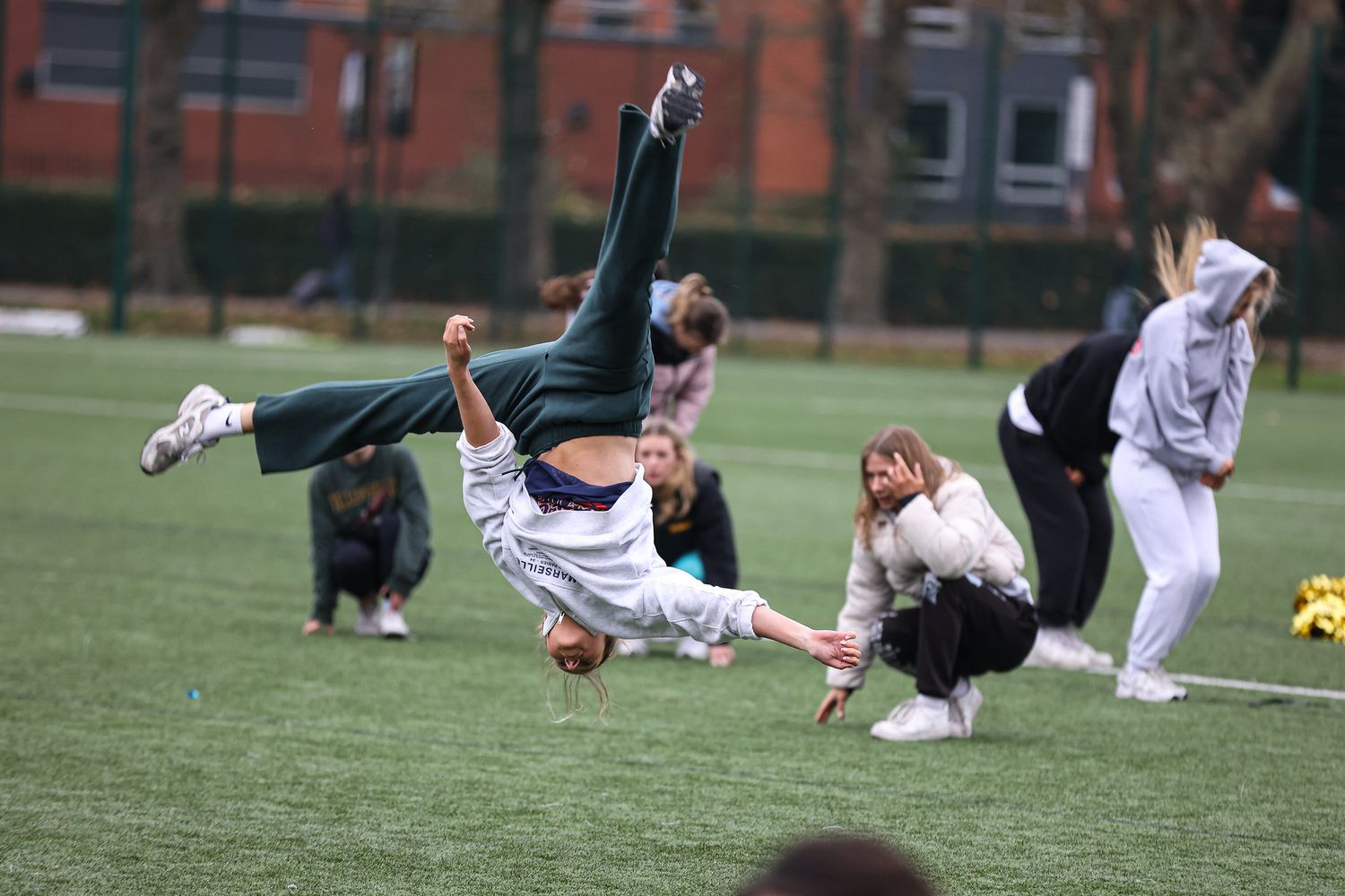 Athletes perform stretching exercises on a green turf field during a group training session.