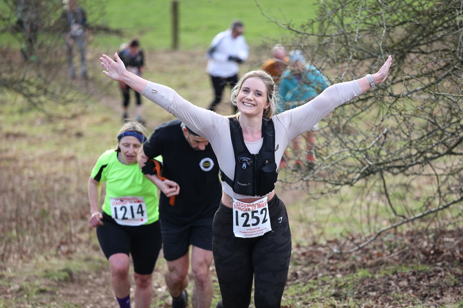 Cross country runners showing enthusiasm while racing through a natural trail course.