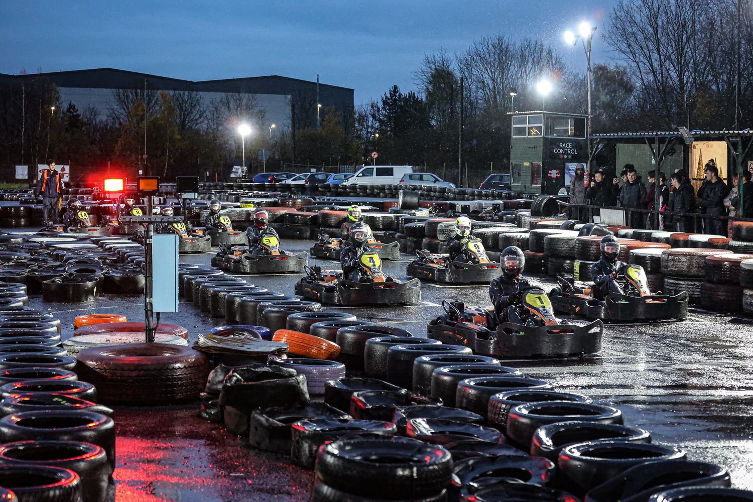 Cars parked in a dark parking lot illuminated by bright overhead lights on a rainy evening.