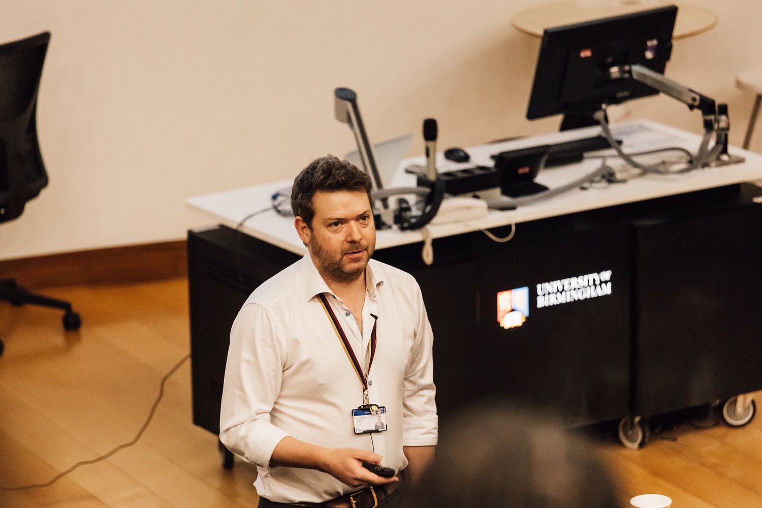 A presenter speaks at a podium with technology equipment in a professional setting.