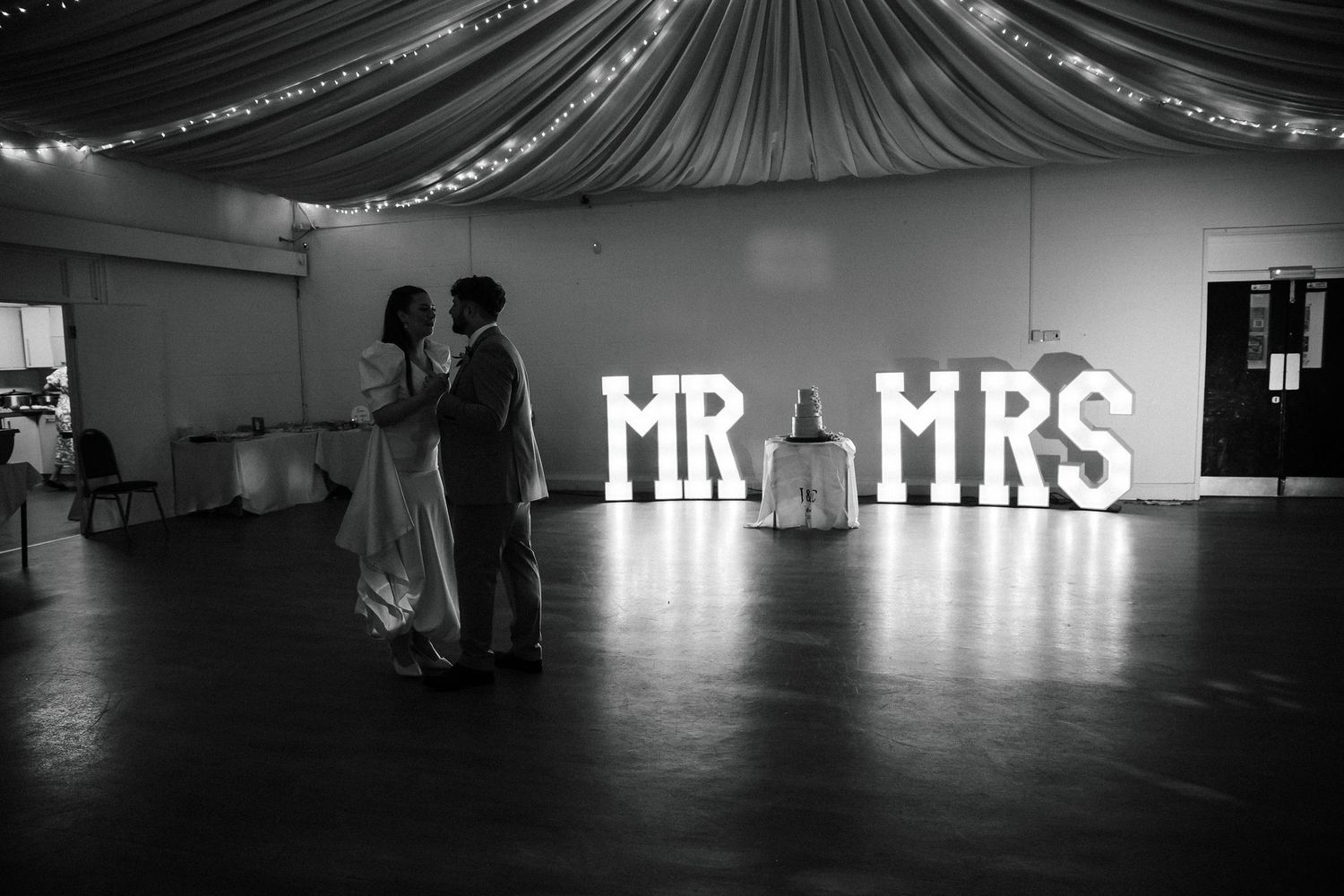 Couple shares first dance in front of illuminated MR & MRS marquee letters at wedding reception.