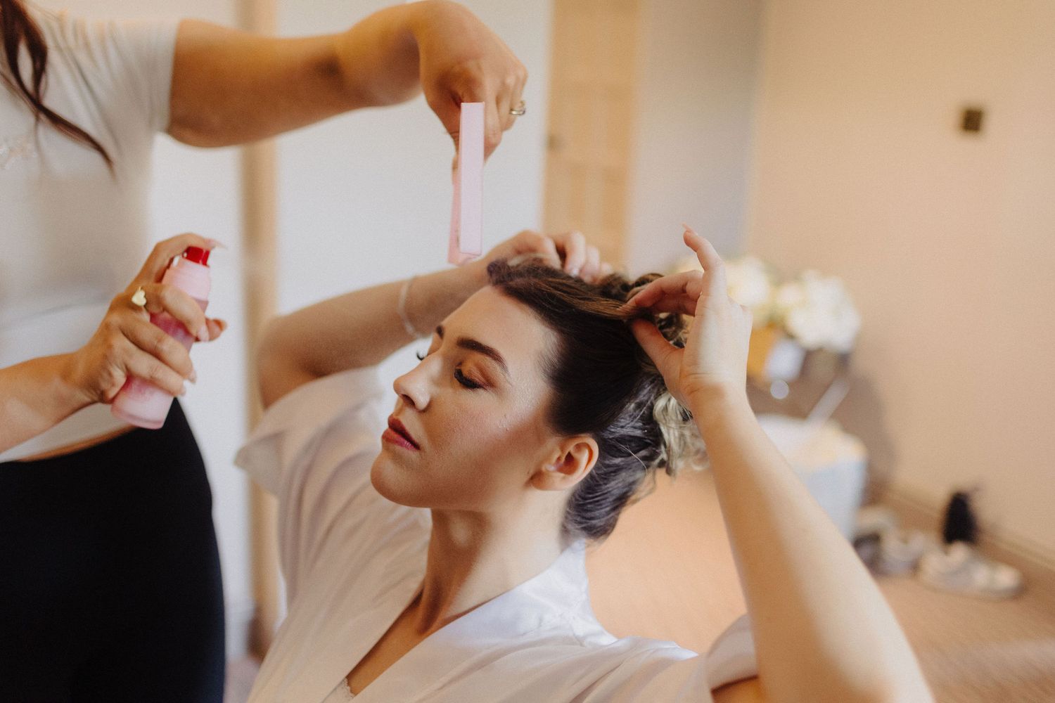 Bride getting hair styled by professional hairstylist with spray before wedding ceremony.
