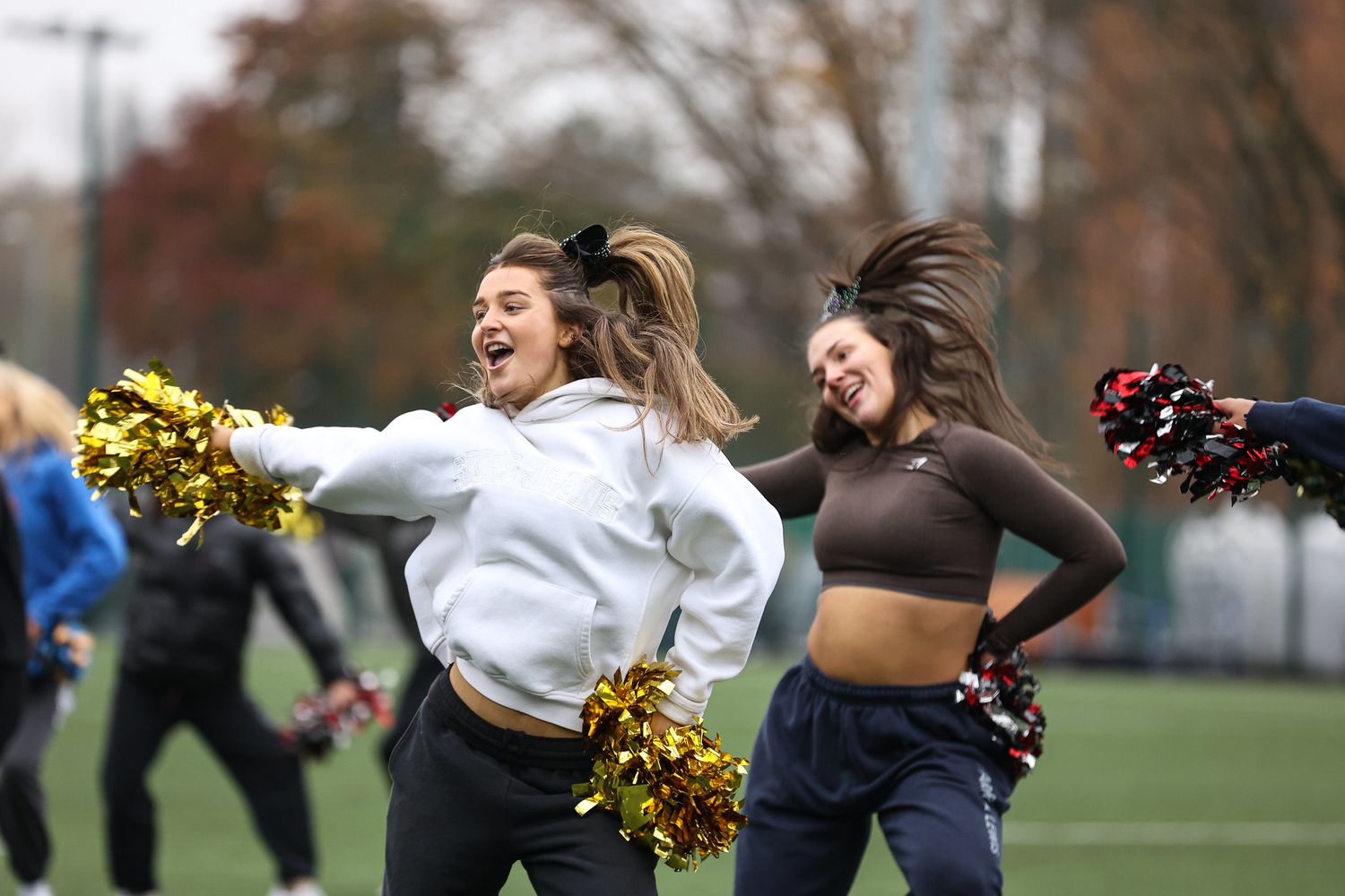Cheerleaders perform energetic dance routines during an outdoor sporting event on a fall day.