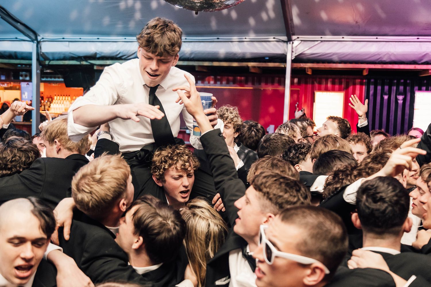 Crowded concert or club scene with colorful lighting and energetic atmosphere.