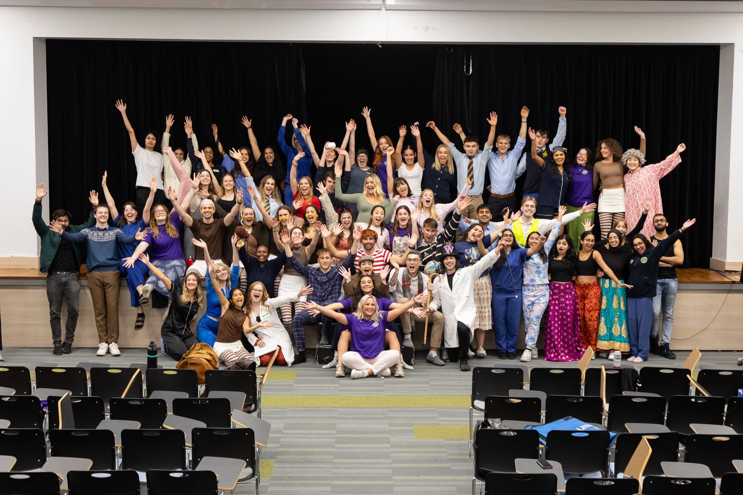 Audience members in an auditorium raise their hands enthusiastically during a performance.