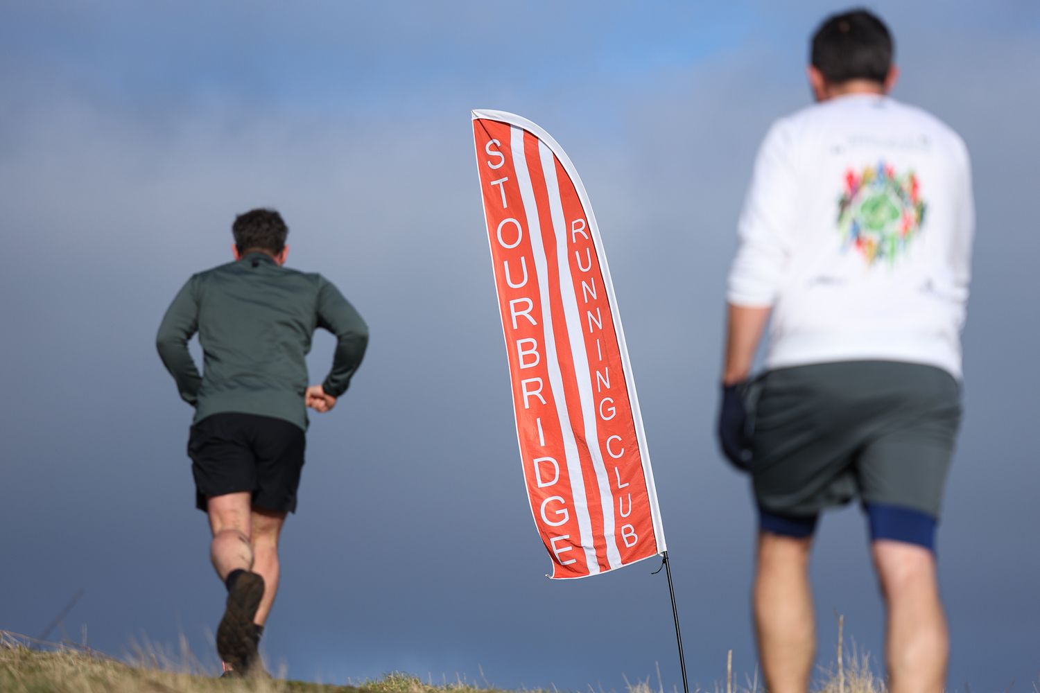 Athletes running along a scenic trail with a dramatic cloudy sky backdrop.