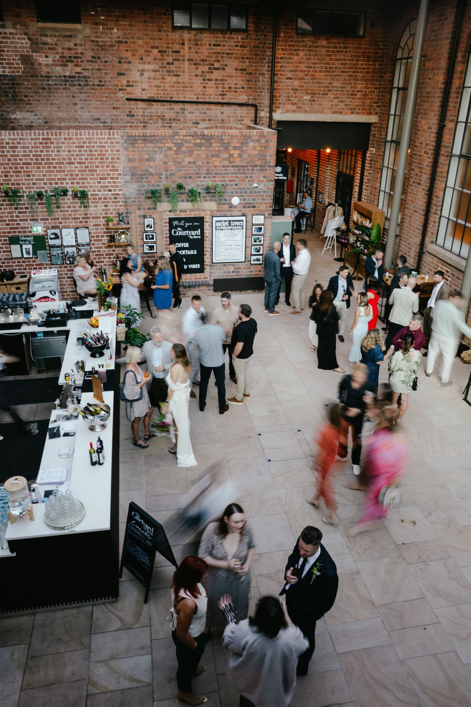 Aerial view of wedding reception guests mingling in a rustic brick venue with a bar and dance floor.