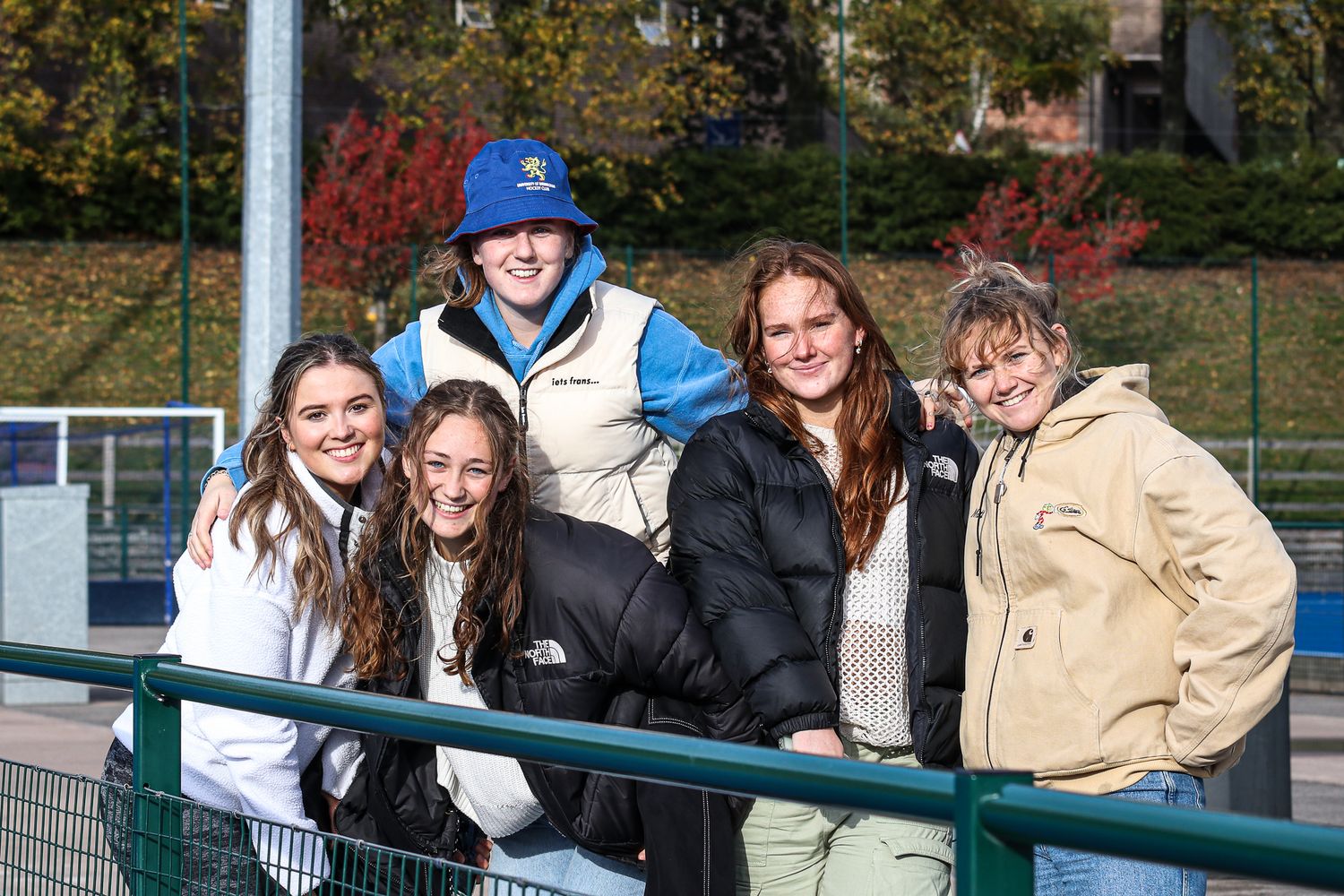 Spectators gathered along a railing watching a sporting event on a sunny autumn day.