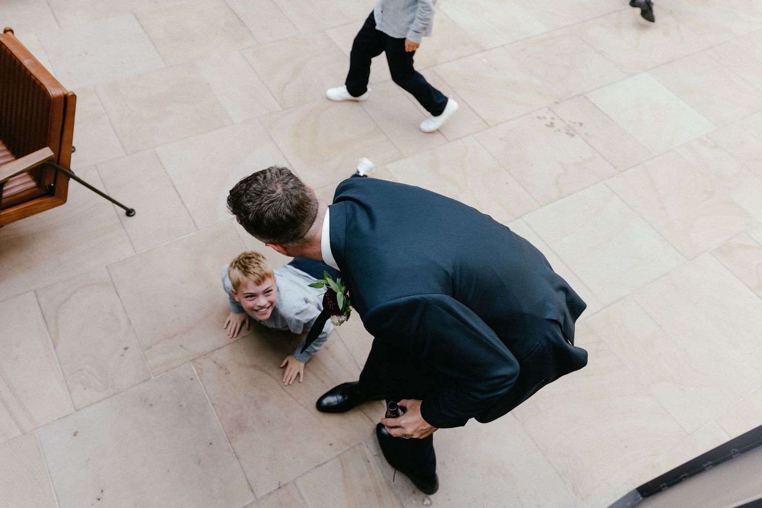 Man in suit bending down to interact with smiling toddler on marble floor at formal event.