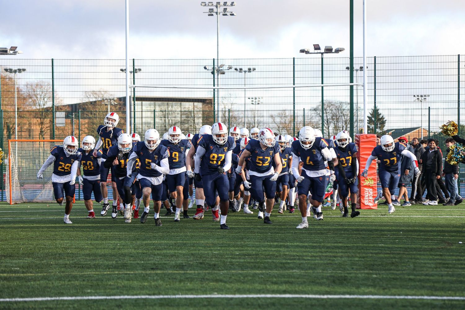 Athletes participate in football training drills on multiple outdoor turf fields during a sports camp session.