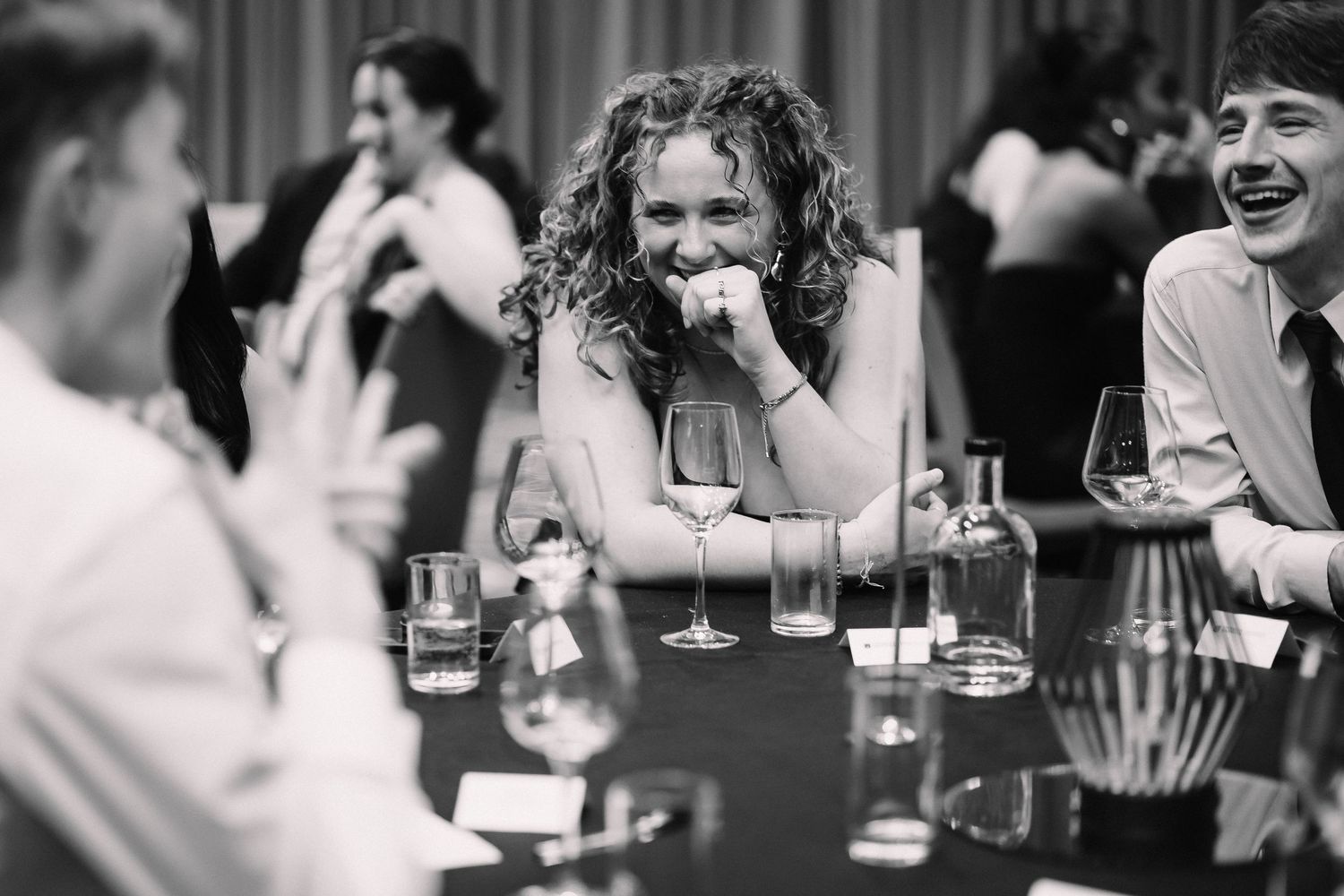 Black and white photo of people gathered at a dining table engaged in lively conversation.