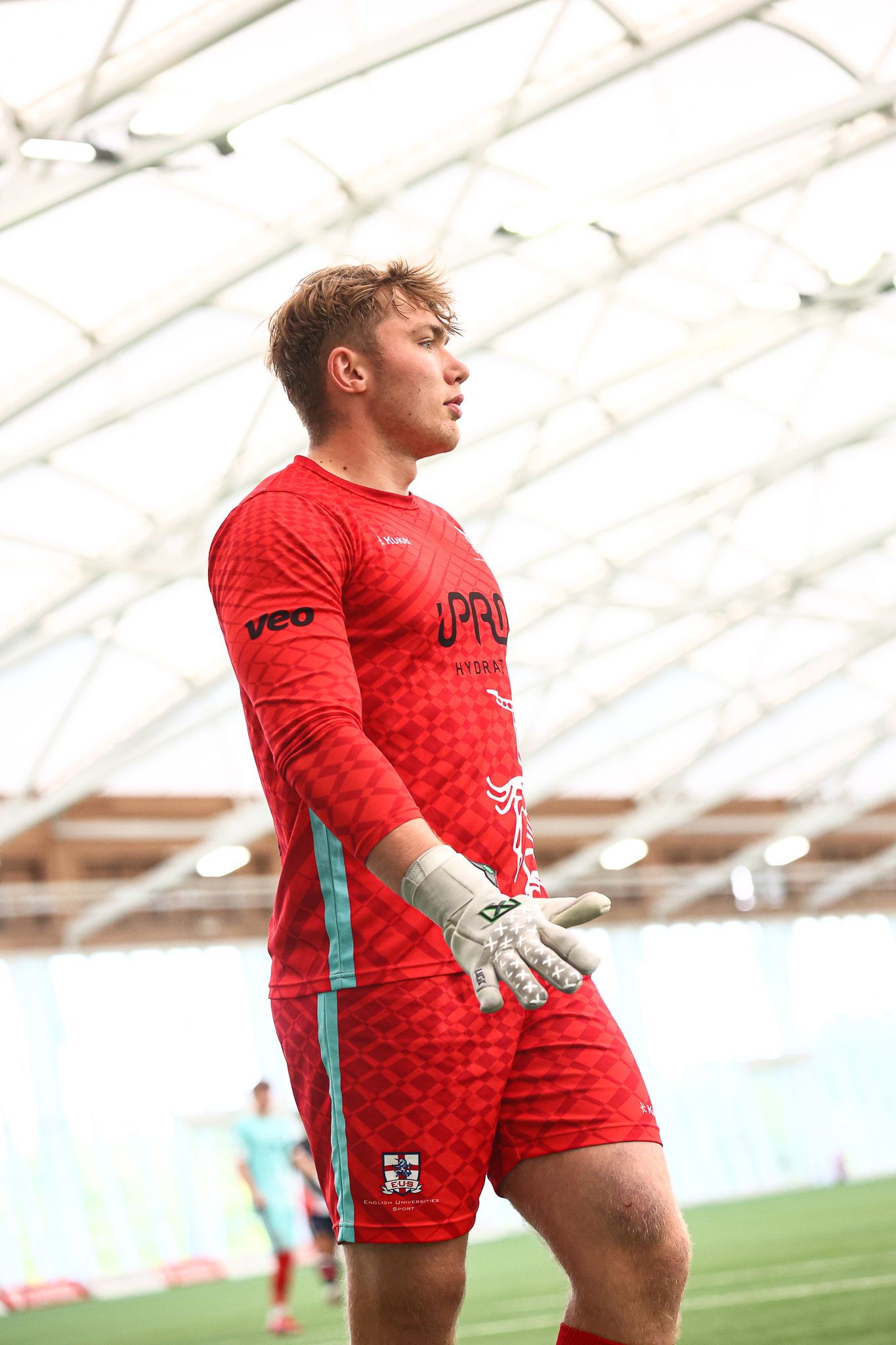 Goalkeepers in red jerseys training on indoor soccer field.