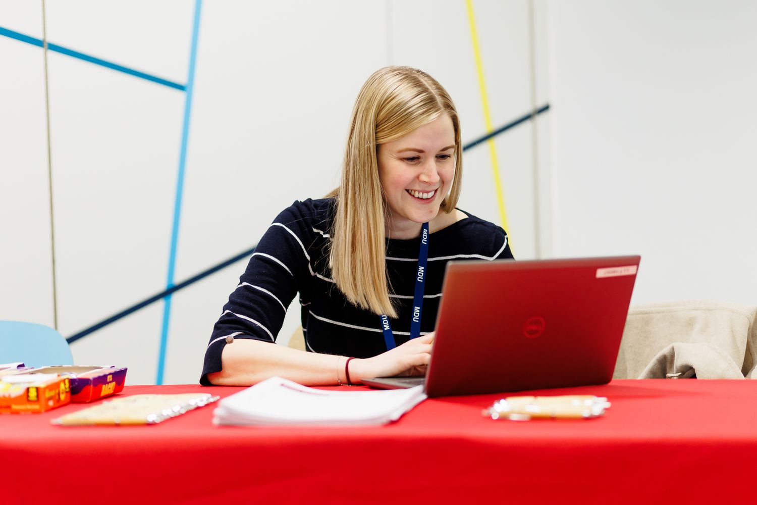 Student works on a red table with a laptop in a bright modern space.