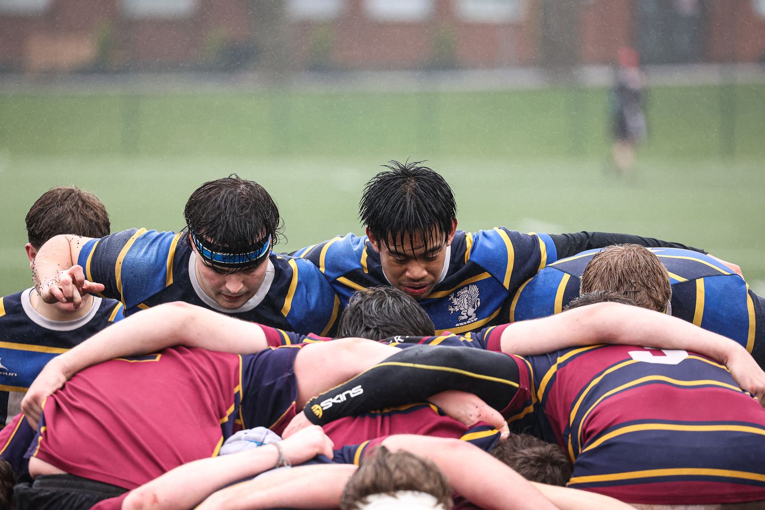 Rugby teams lock into a scrum formation on a muddy field.