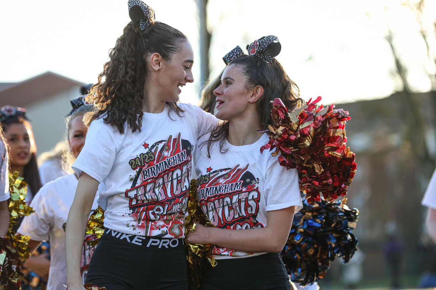 Dance team performs energetic choreography with red and gold pom poms during an outdoor performance.