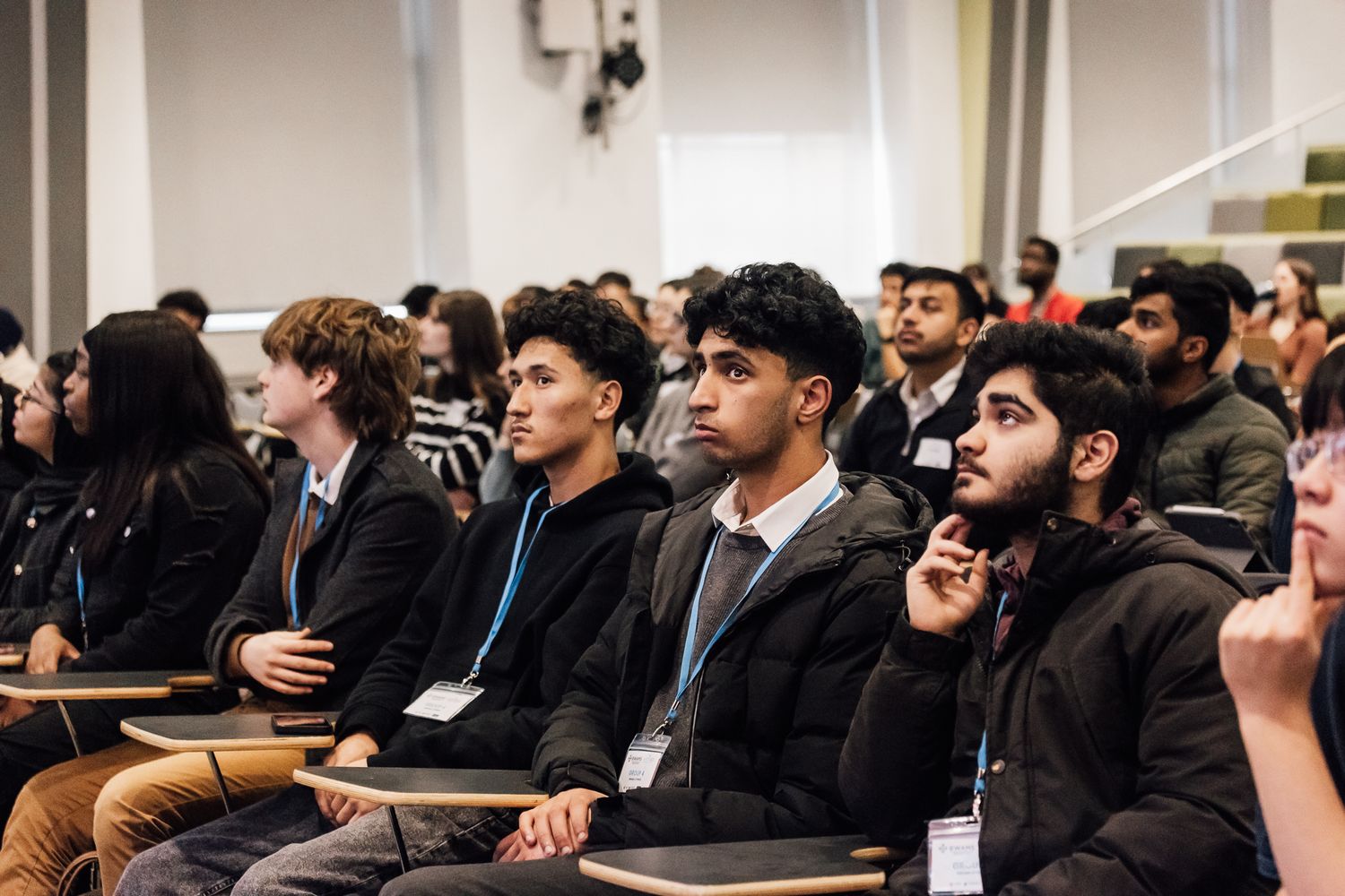 A diverse audience of young professionals attentively listens during a conference presentation.