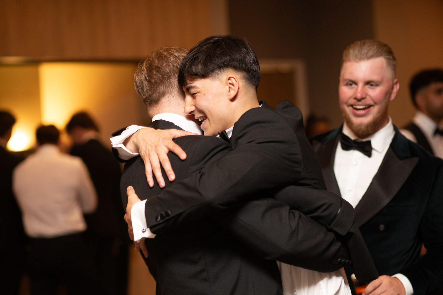 Joyful celebration with people hugging and smiling at a formal indoor gathering.