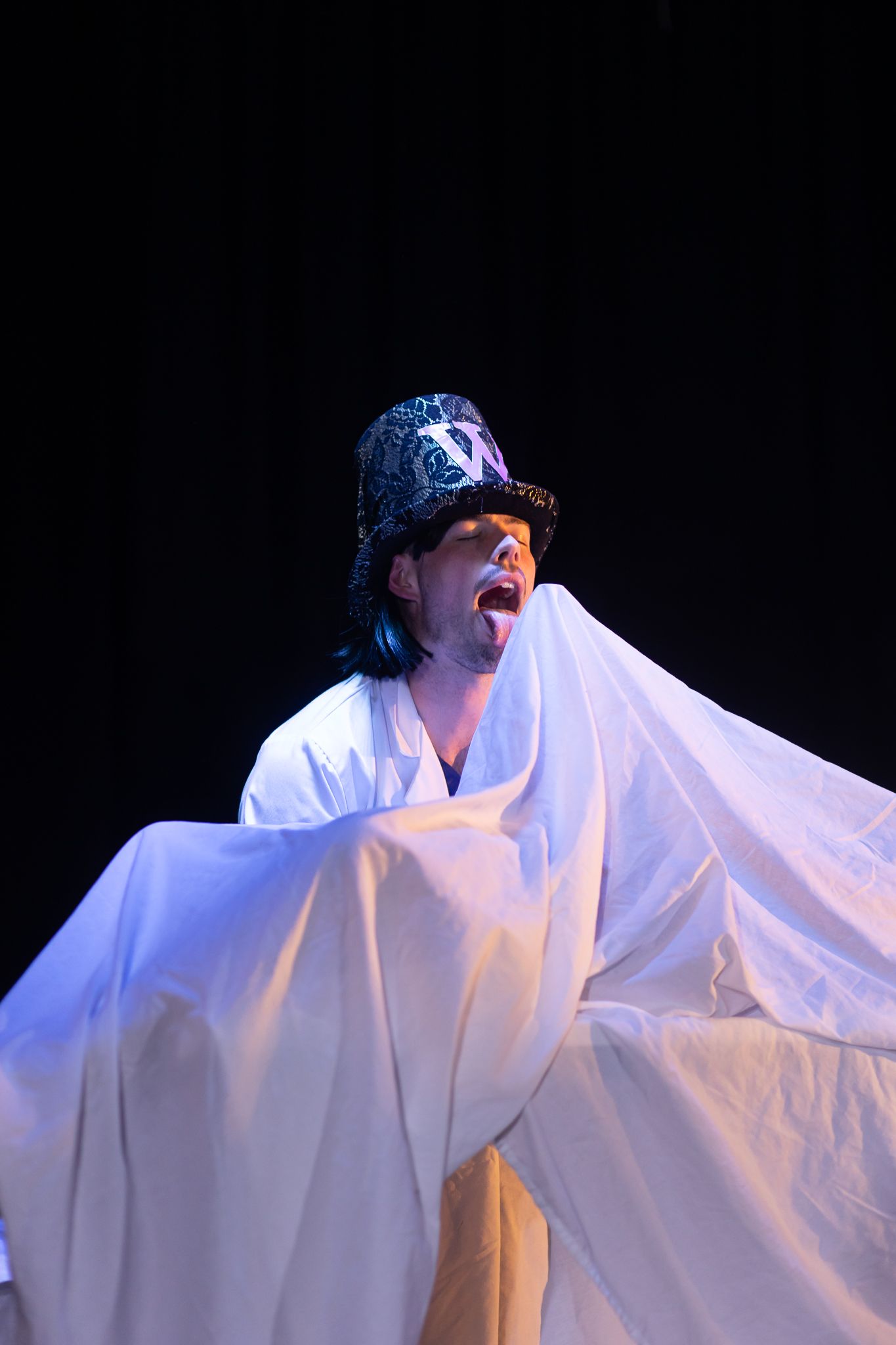 Performer in white ghostly costume dramatically poses against dark background.