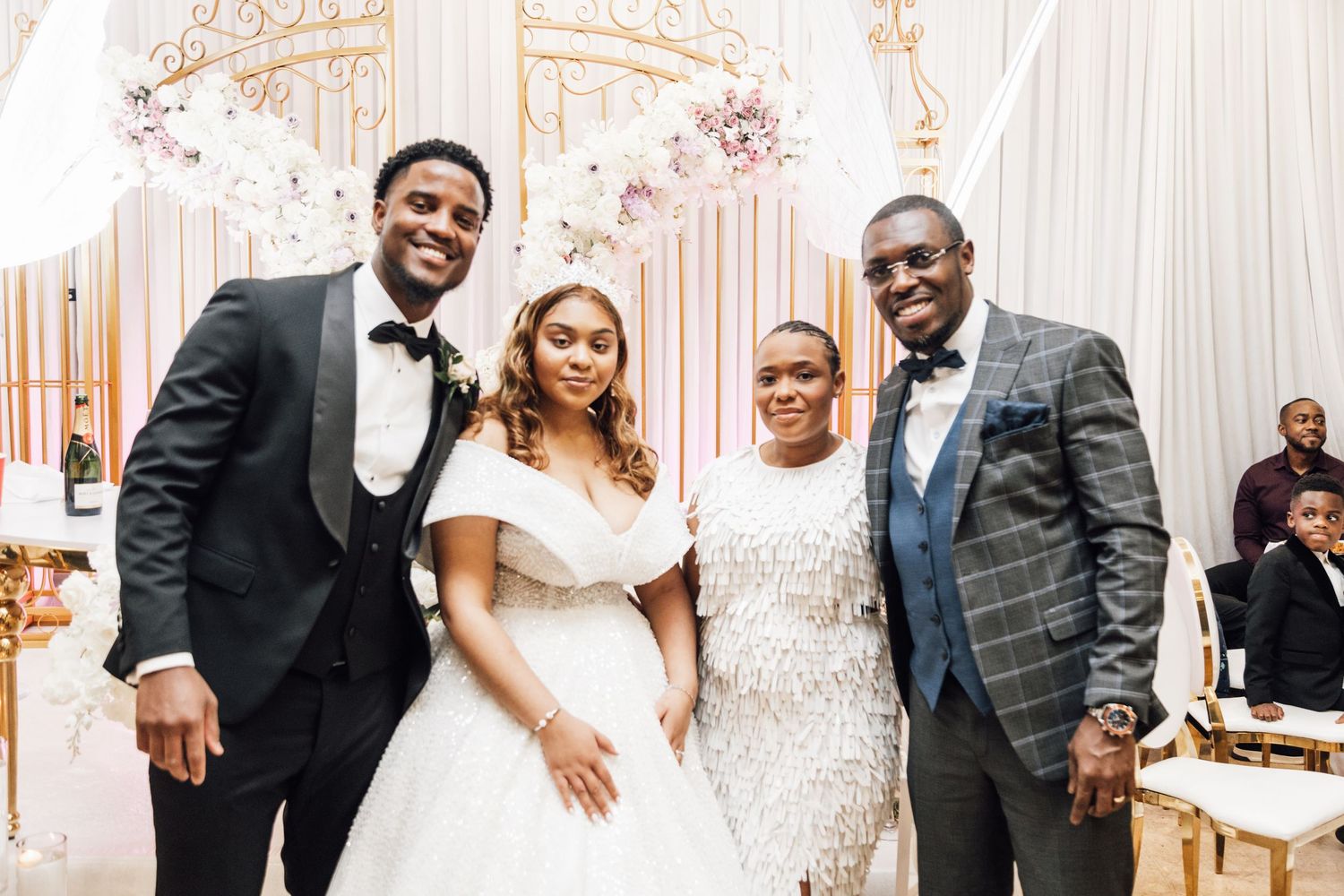Wedding party celebrates in front of elegant white and pink floral backdrop.