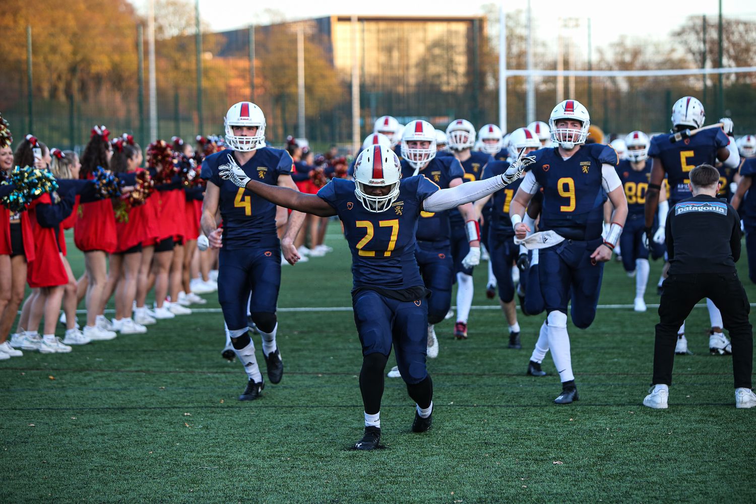 Football players in red and navy uniforms practicing drills on a grass field during an autumn afternoon practice session.