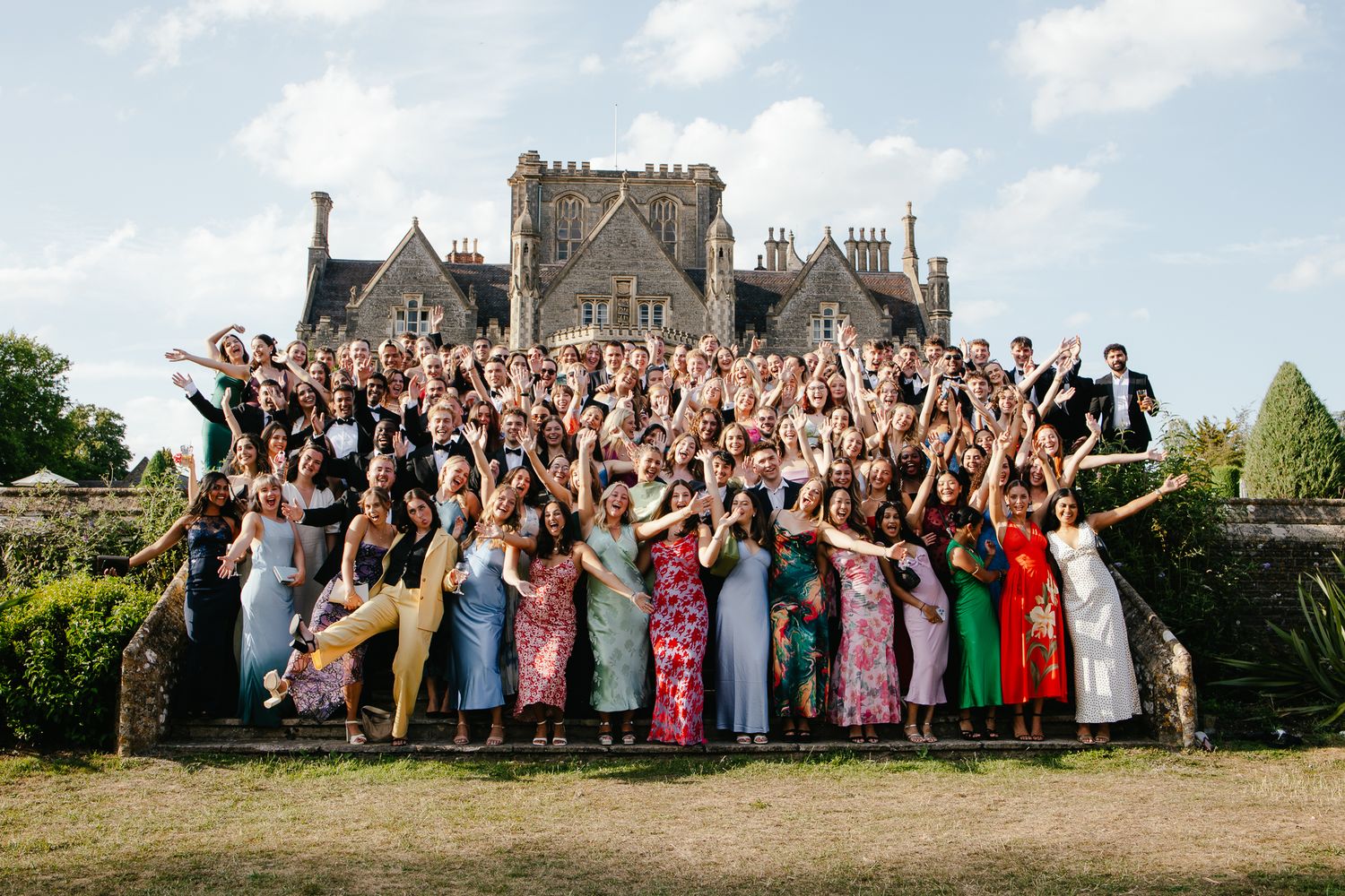 Large group of wedding guests posing together in front of a grand stone castle during a celebration.
