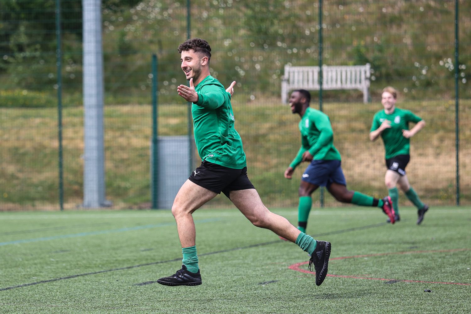 Athletes in green uniforms running and jumping during a soccer practice session.