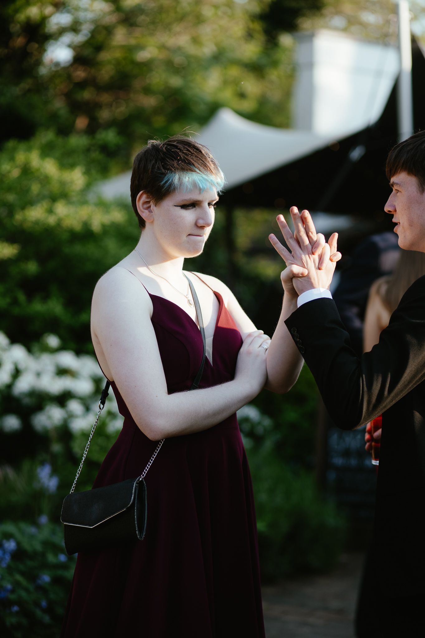 Person in burgundy formal wear gestures animatedly during an outdoor gathering.