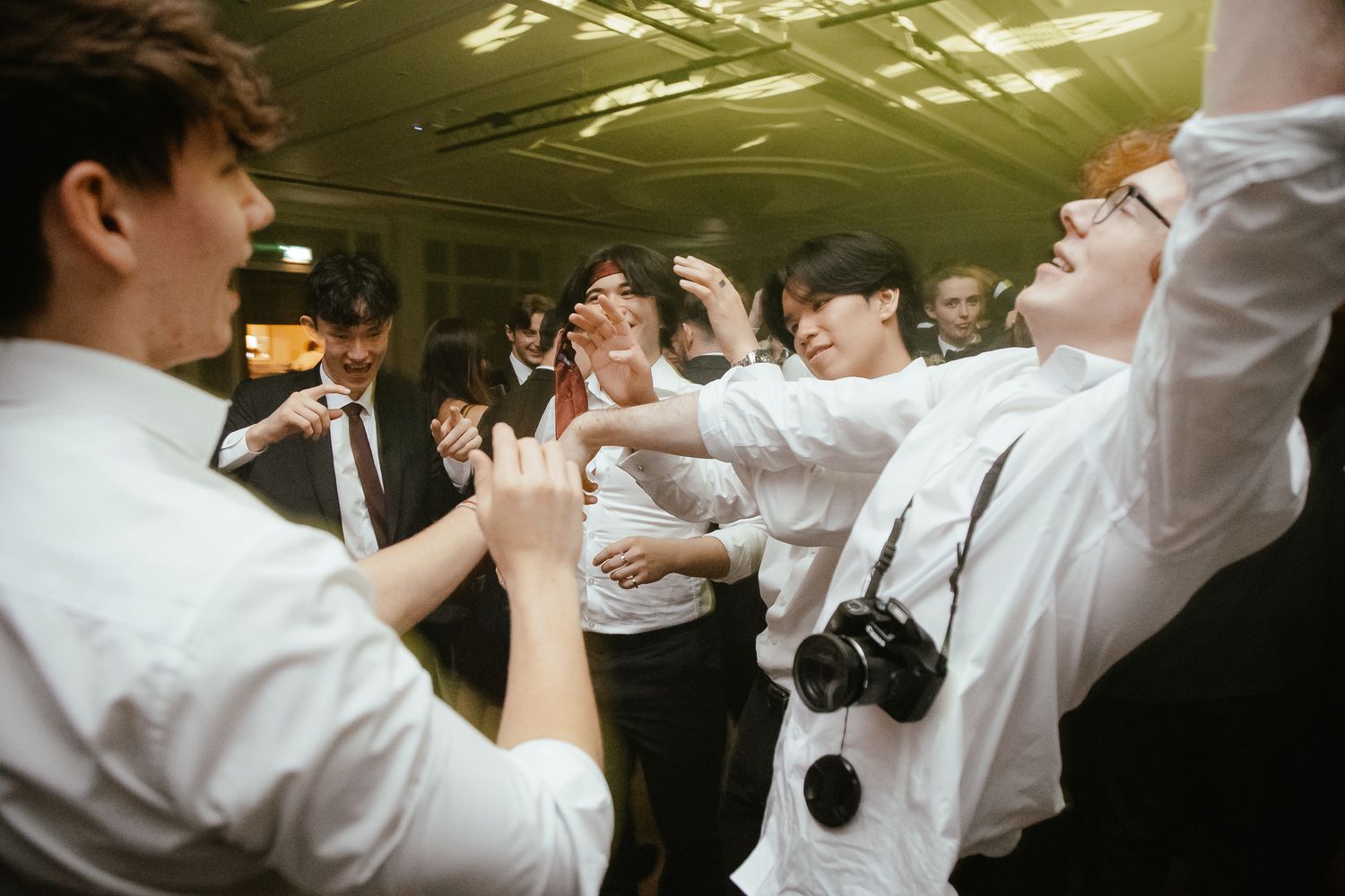 Wedding celebration with guests in white shirts dancing and jumping on the dance floor.