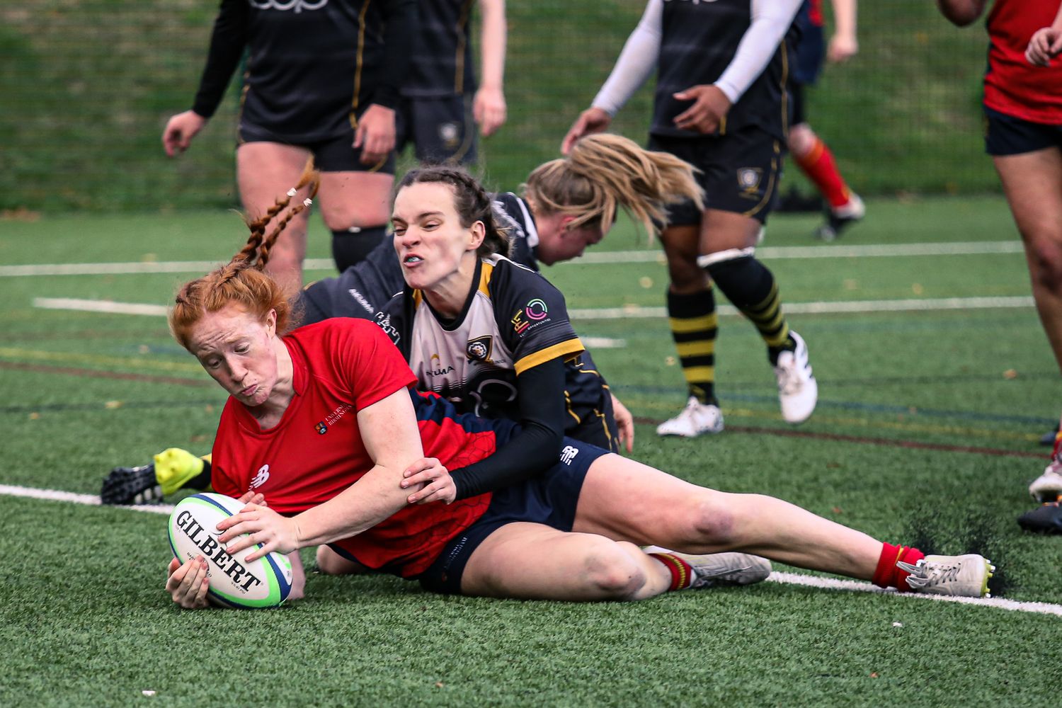 Rugby players diving and tackling during an intense match play on an outdoor field.