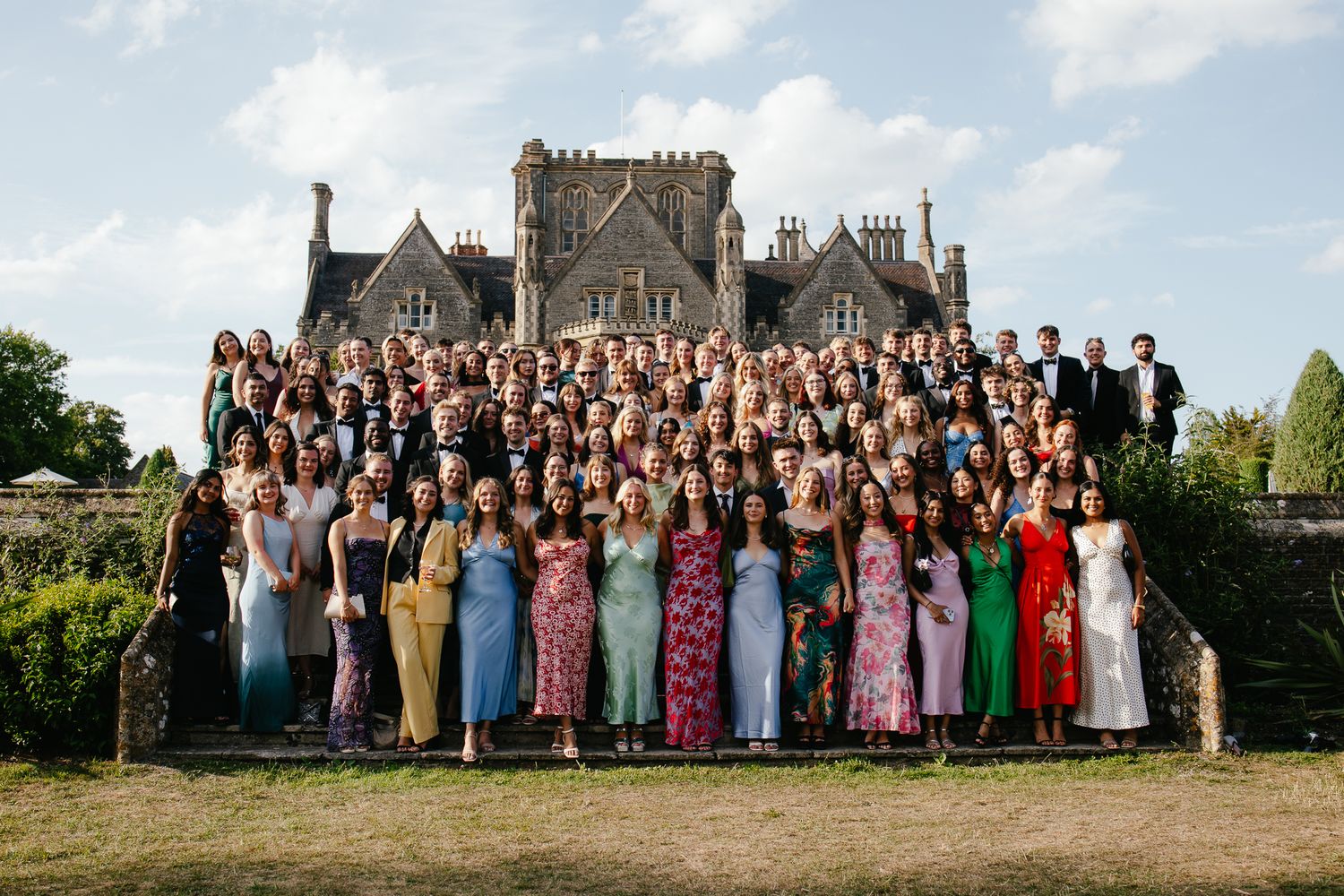 Wedding party group photo with colorful attire in front of historic stone building.