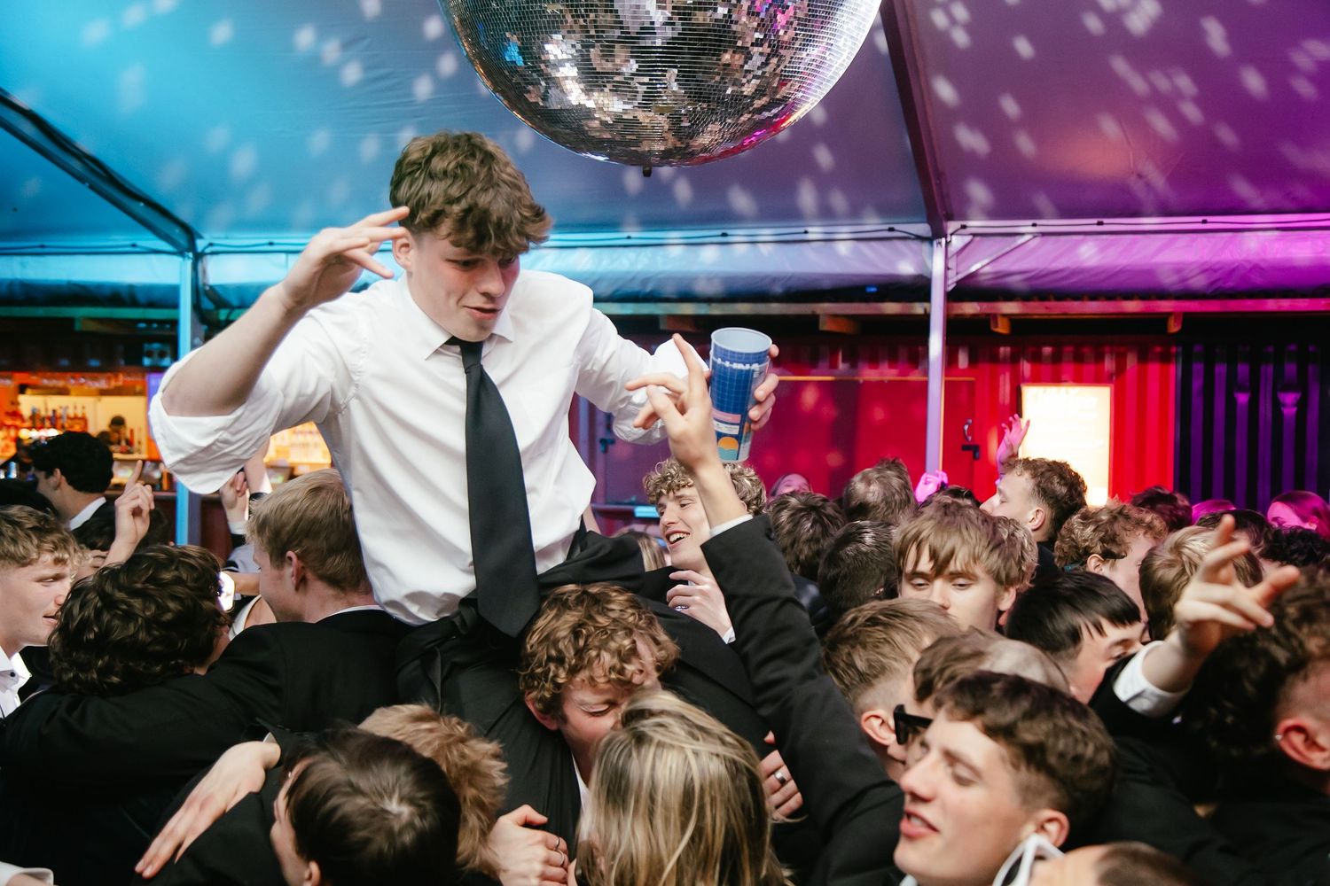 Lively dance party scene under a disco ball with colorful purple and blue lighting.