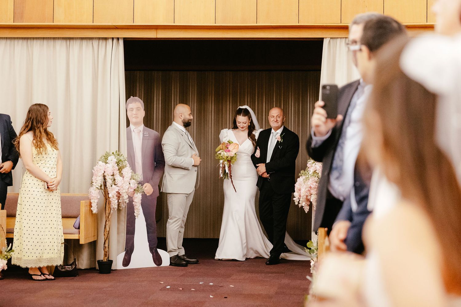 Bride walking down the aisle with escorts during a wedding ceremony in a warmly lit venue.