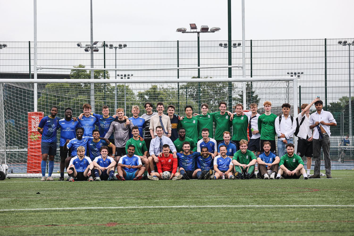 Teams sitting together on the sidelines of a soccer field watching the game.