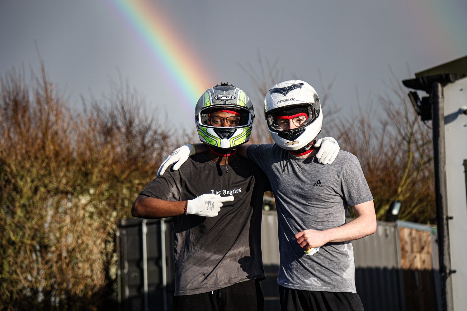 Rainbow arches over a group of motorsport racers wearing helmets and safety gear.