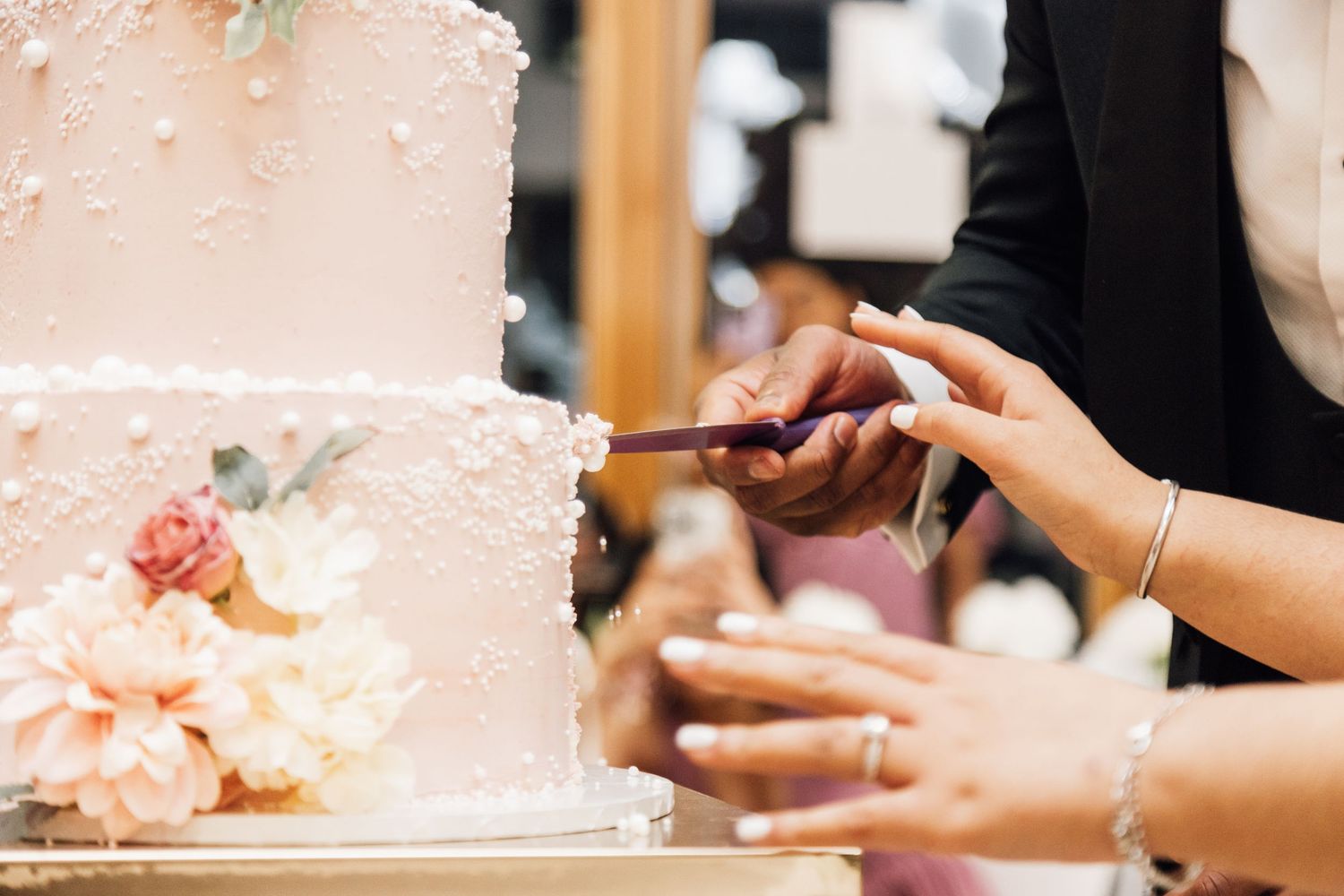 Close-up of delicate pink floral details on multi-tiered wedding cake.
