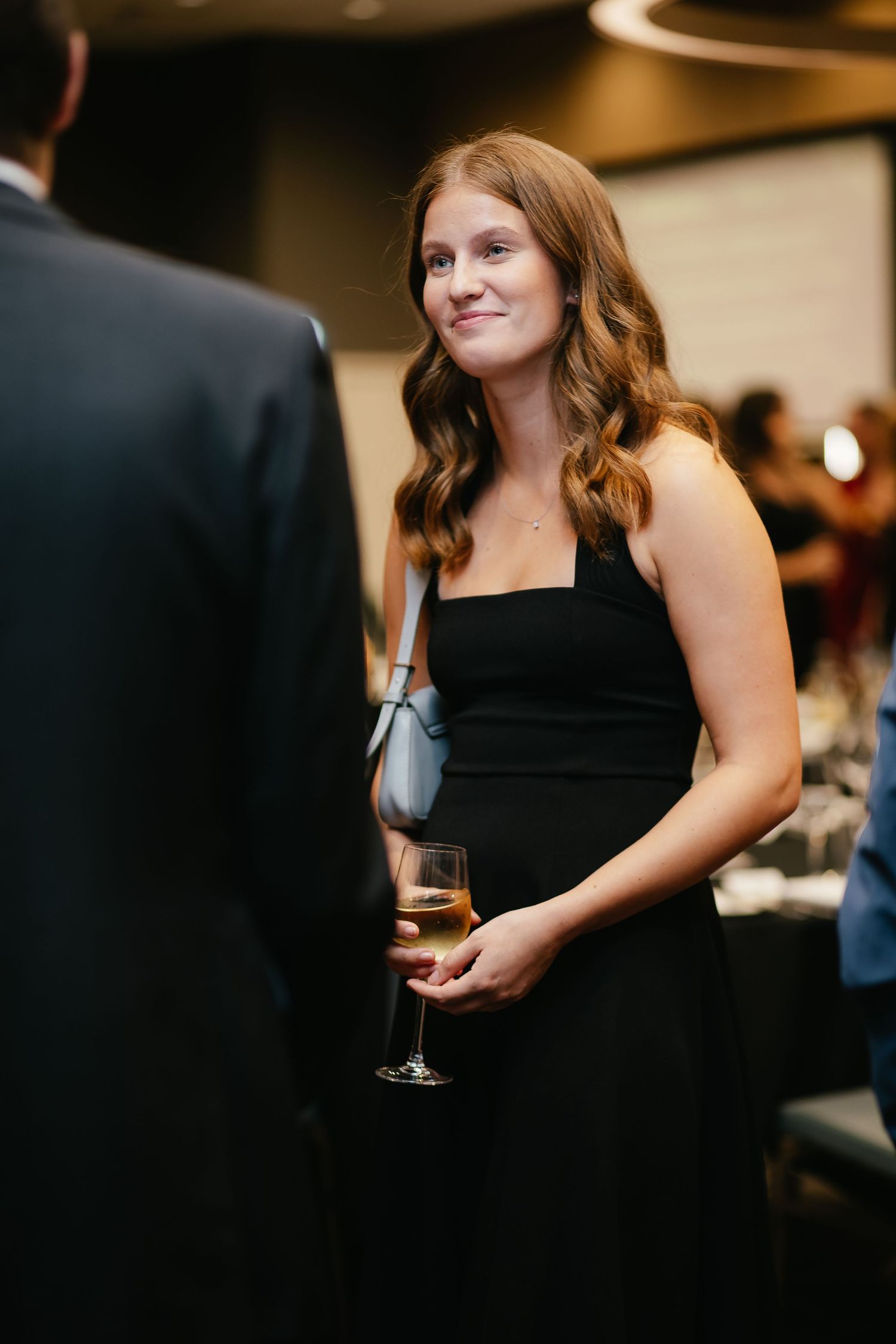Elegant guest in a black formal dress holds a wine glass at an upscale evening event.