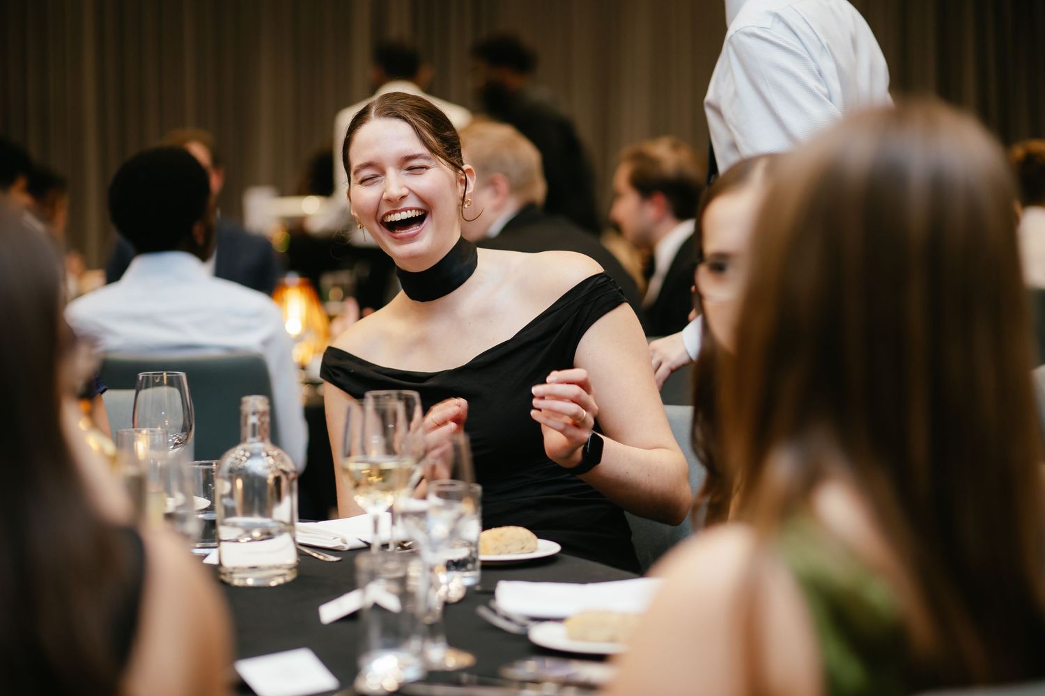Guests enjoy laughter and conversation during an elegant dinner party at a restaurant table.