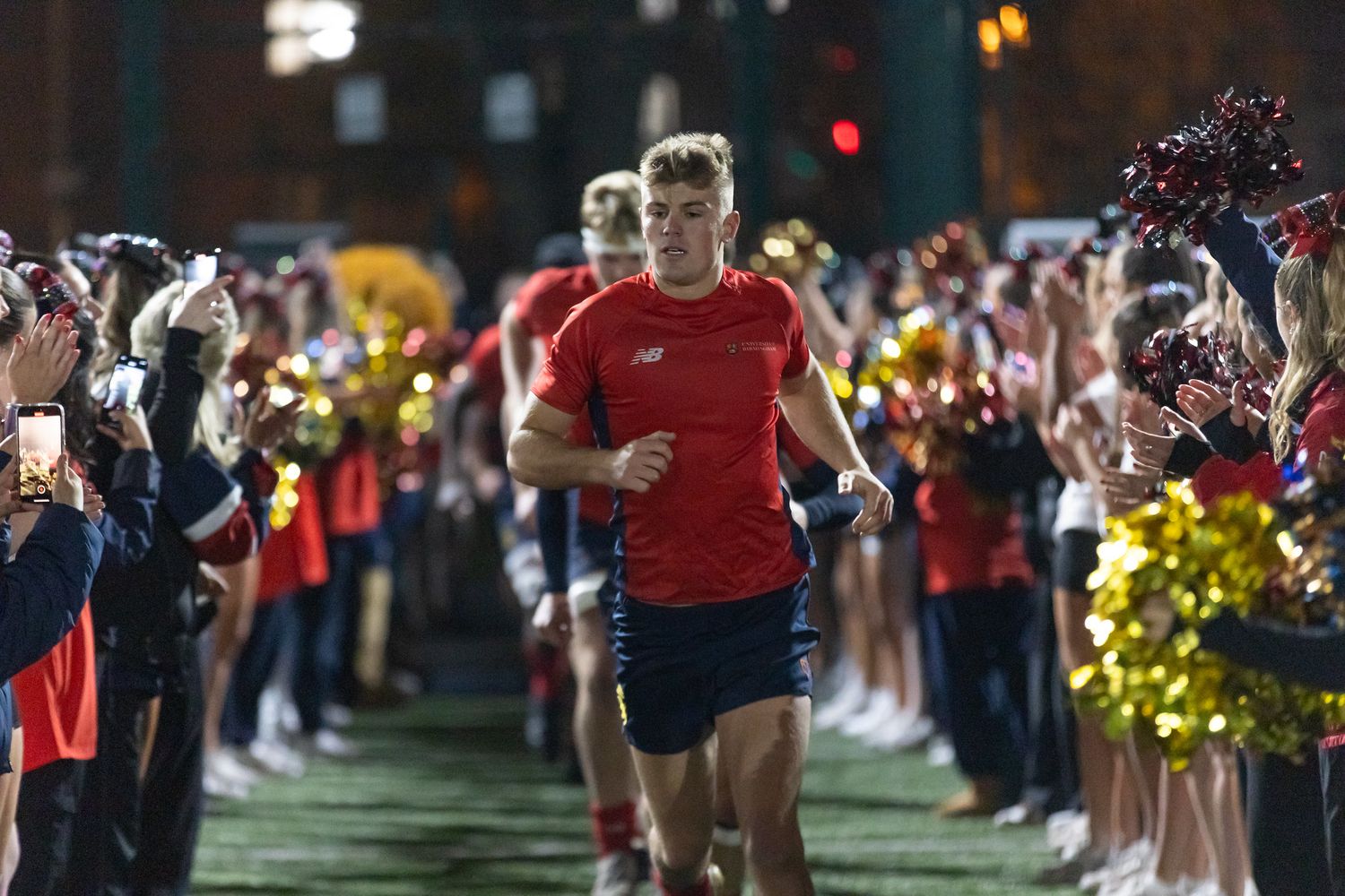 Runners jog along a path at night while spectators line both sides holding glowing lights and cheering.