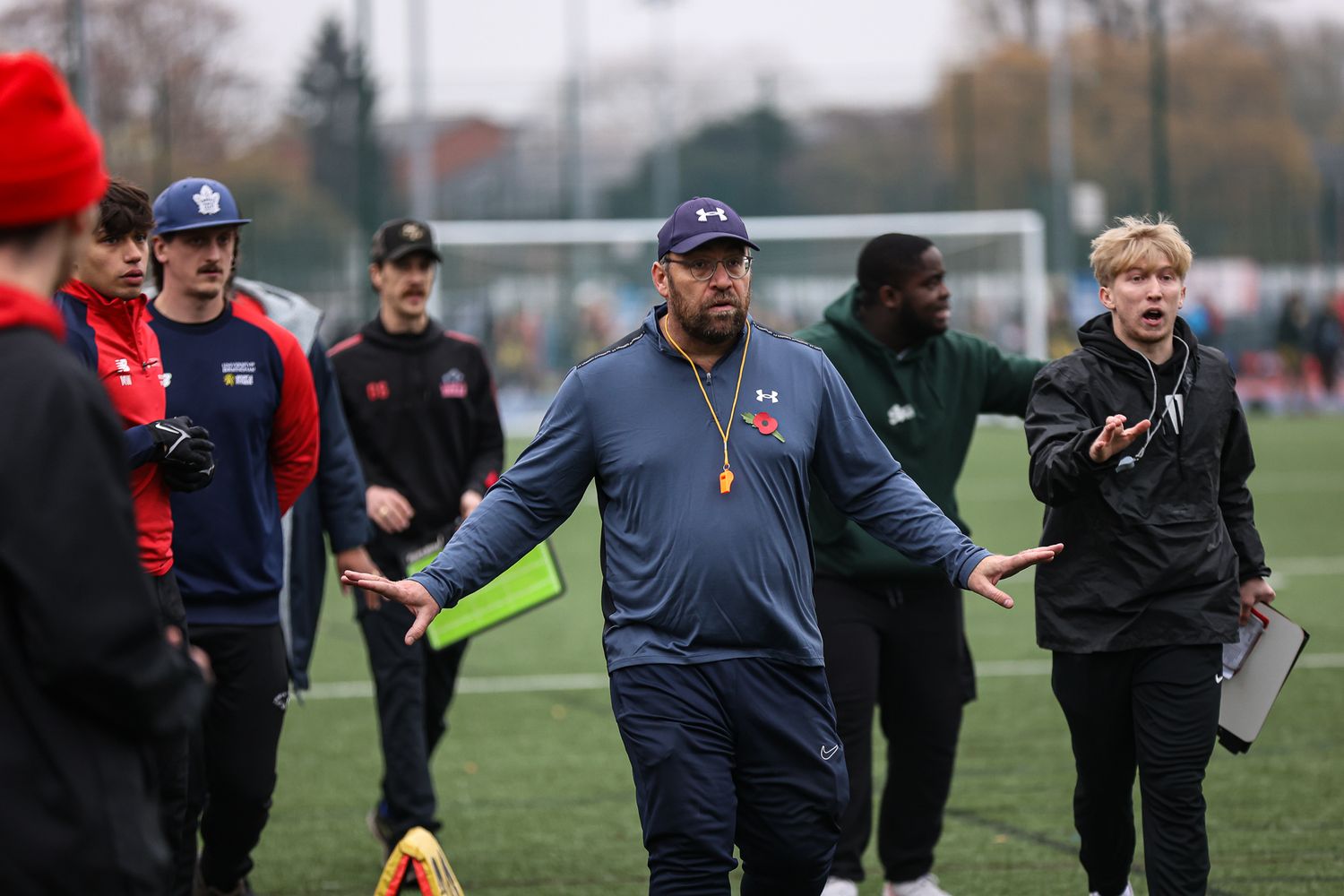 Coaches and players in navy and red uniforms conducting football practice drills.