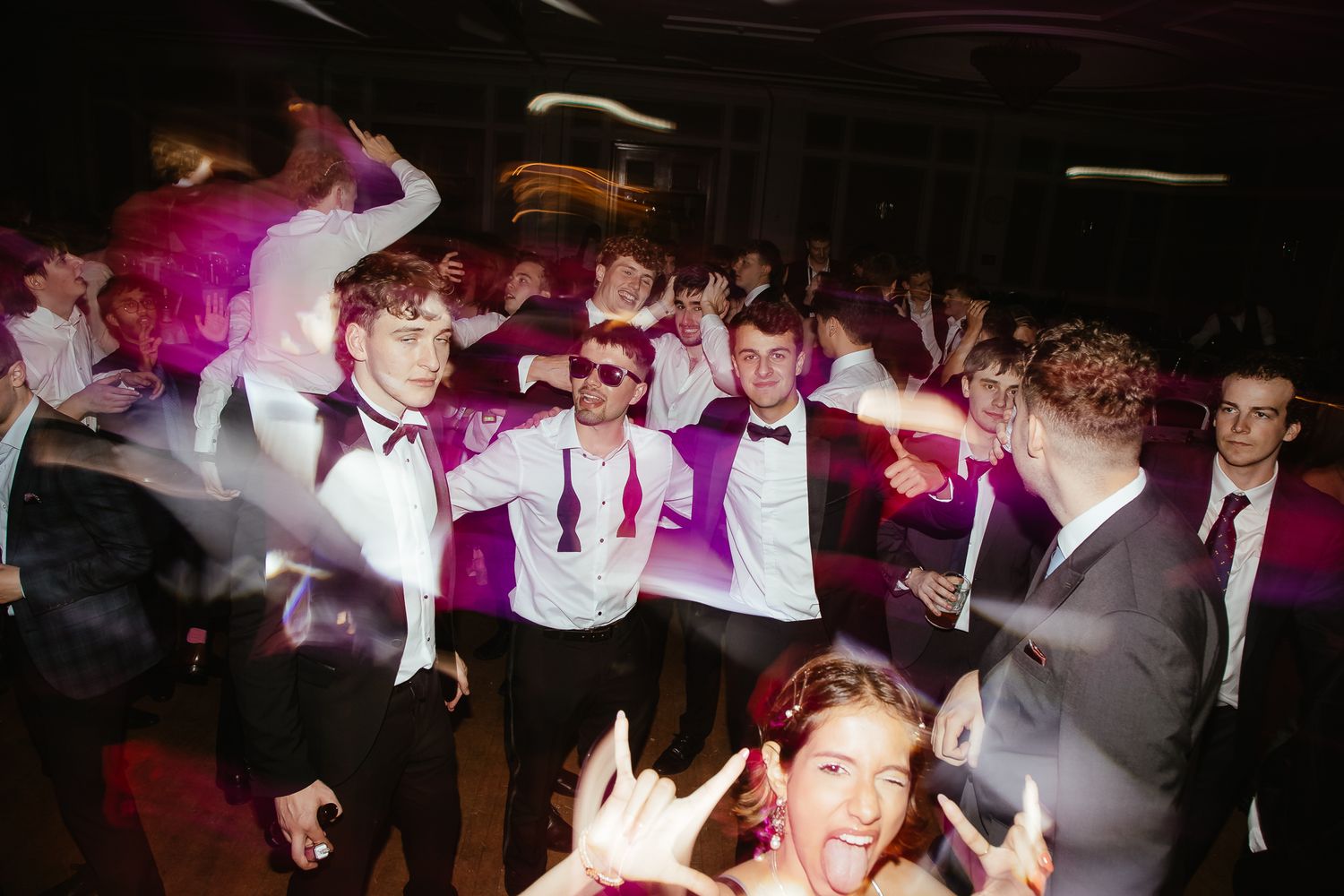Energetic party scene with people dancing and celebrating in a dark room with colorful lighting.