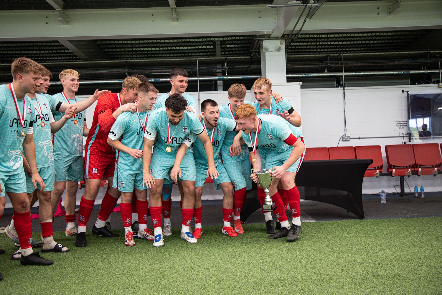 Soccer team lined up on the sidelines during a training session wearing turquoise uniforms.