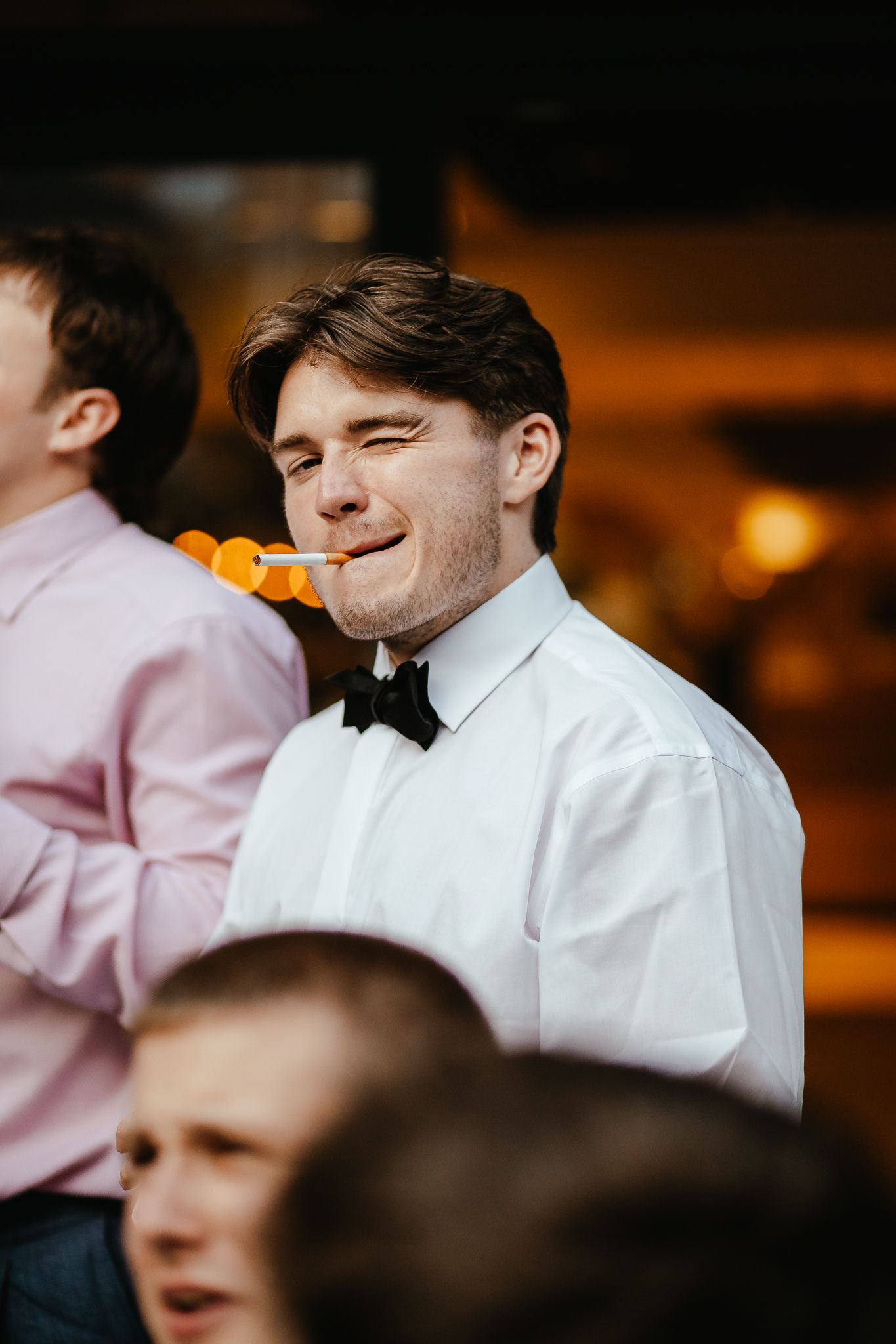 Groomsmen in white shirts and bow ties sharing a light moment at a formal event.