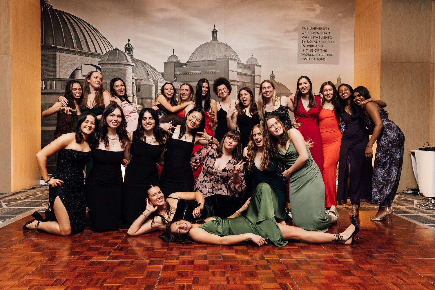 Large group photo with people wearing black outfits sitting on a hardwood floor.