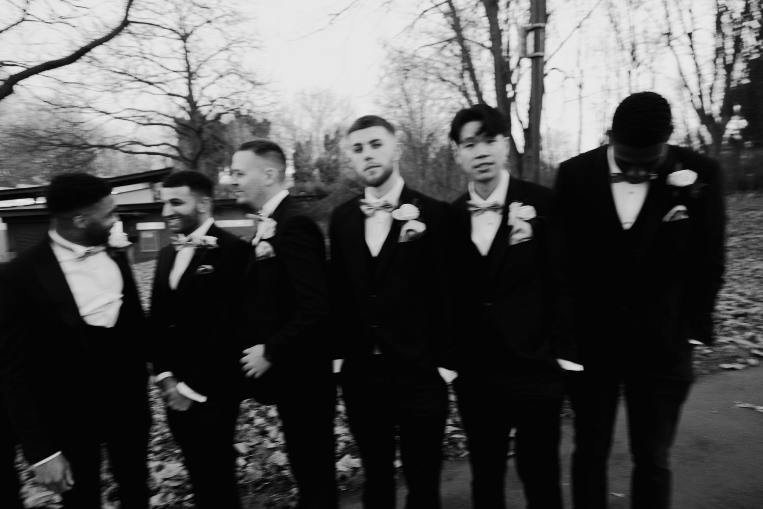 Wedding party in formal black attire posed in a line against bare winter trees.