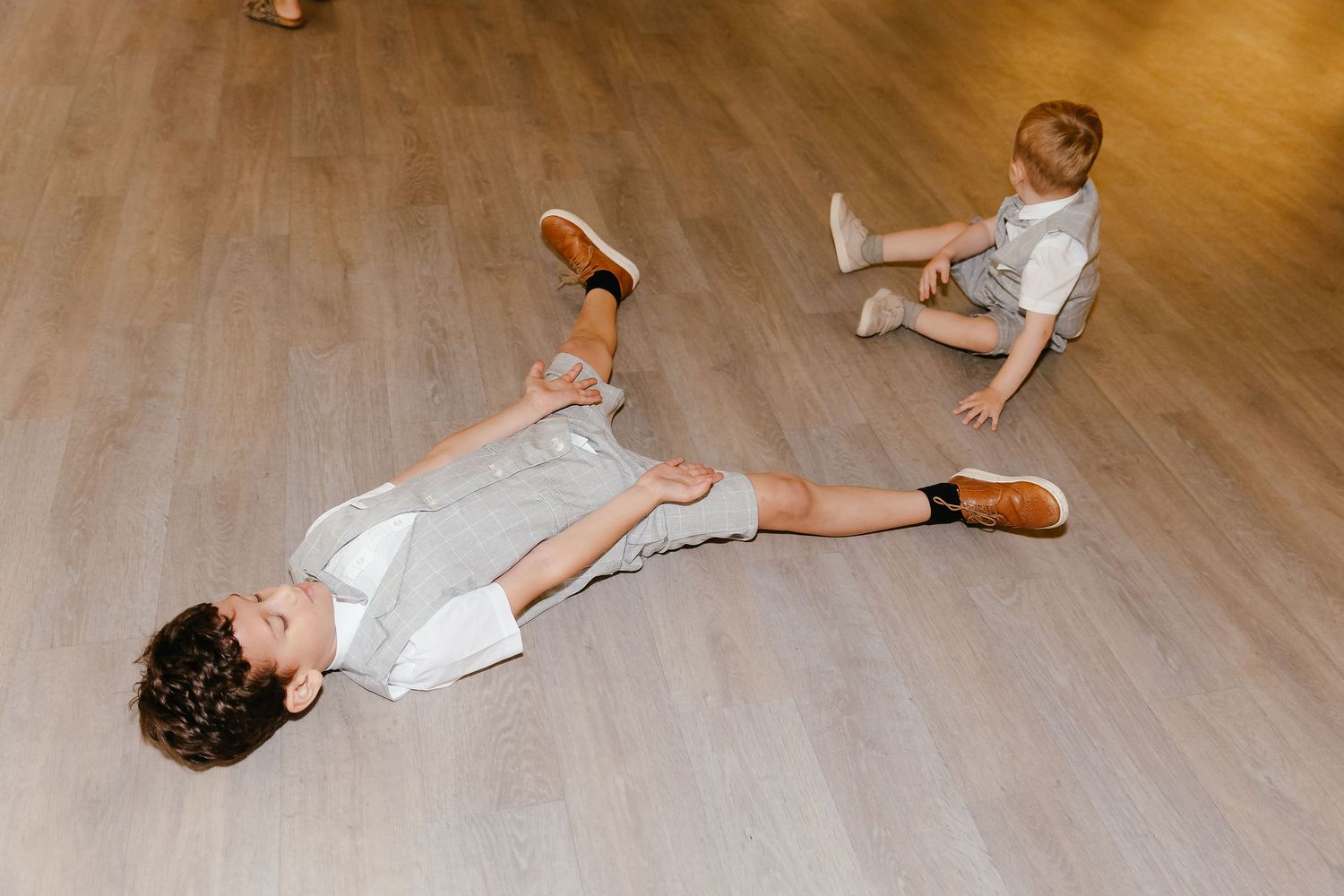 Two young children in matching outfits play on a wooden floor at a wedding.
