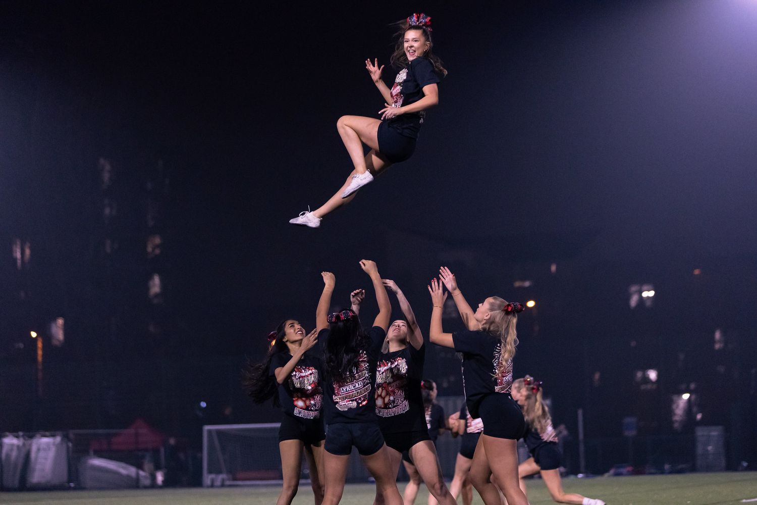 Cheerleaders perform an impressive aerial stunt formation during a nighttime performance.