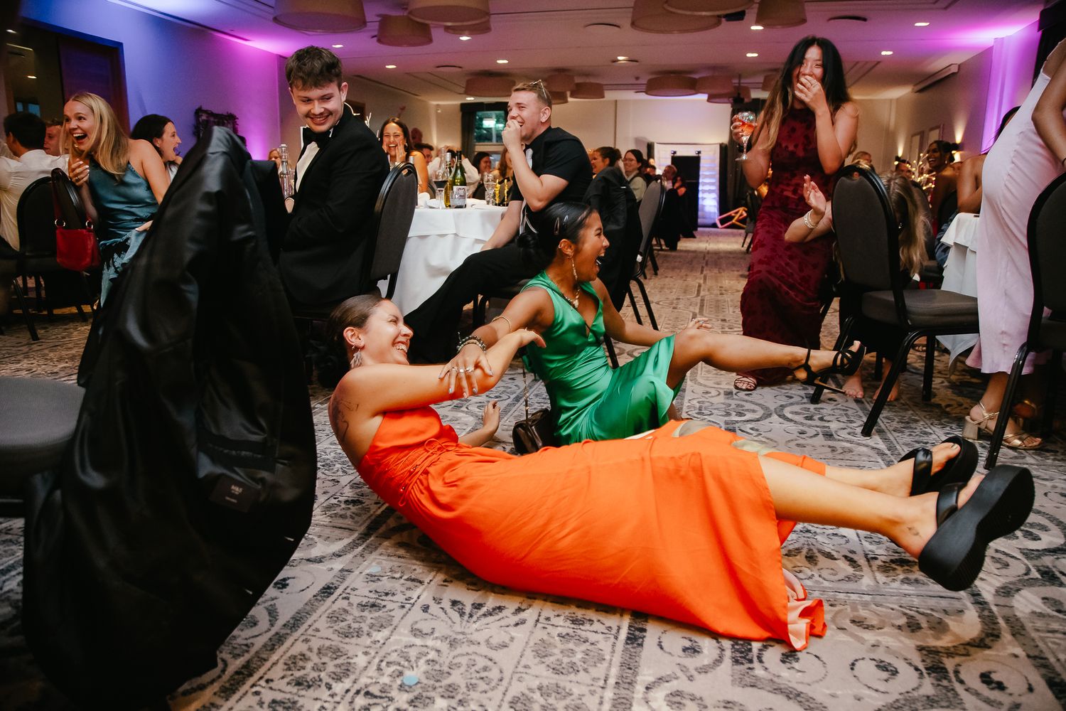 Wedding reception guests dance and celebrate on the floor with vibrant purple lighting overhead at Student Event Photography