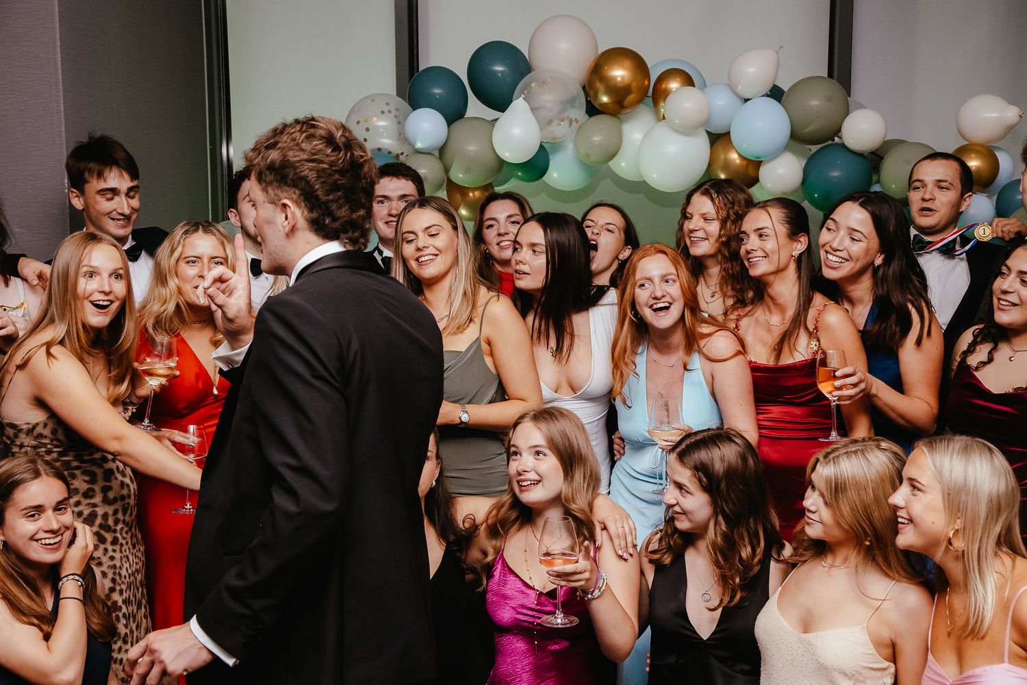 Lively party scene with guests in formal attire dancing under balloon decorations.