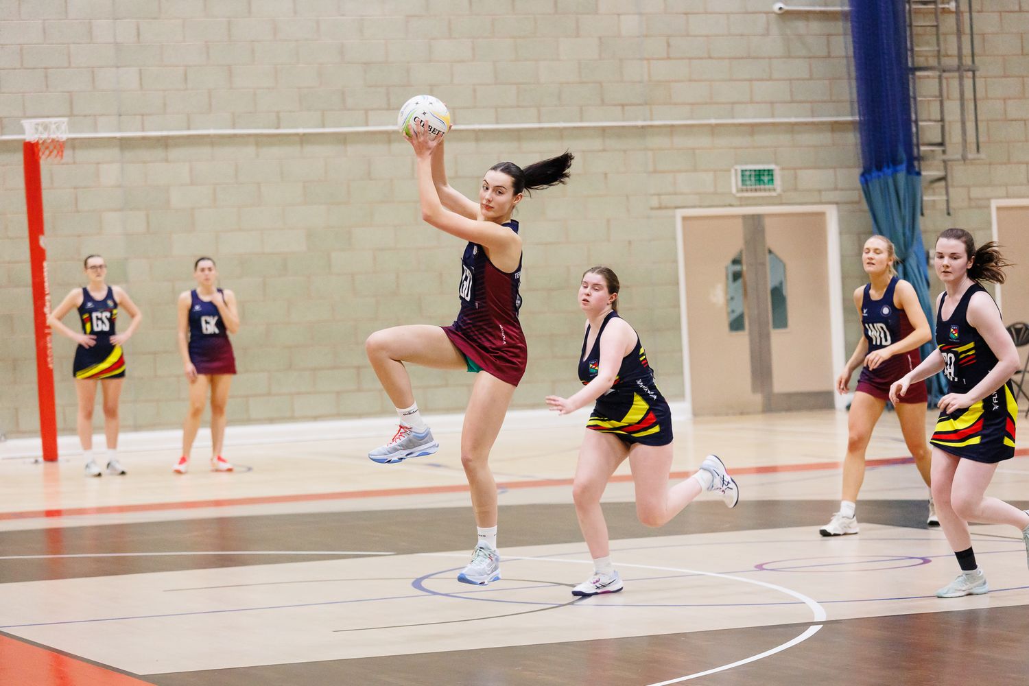 Female athletes playing volleyball in an indoor sports facility with multiple courts.