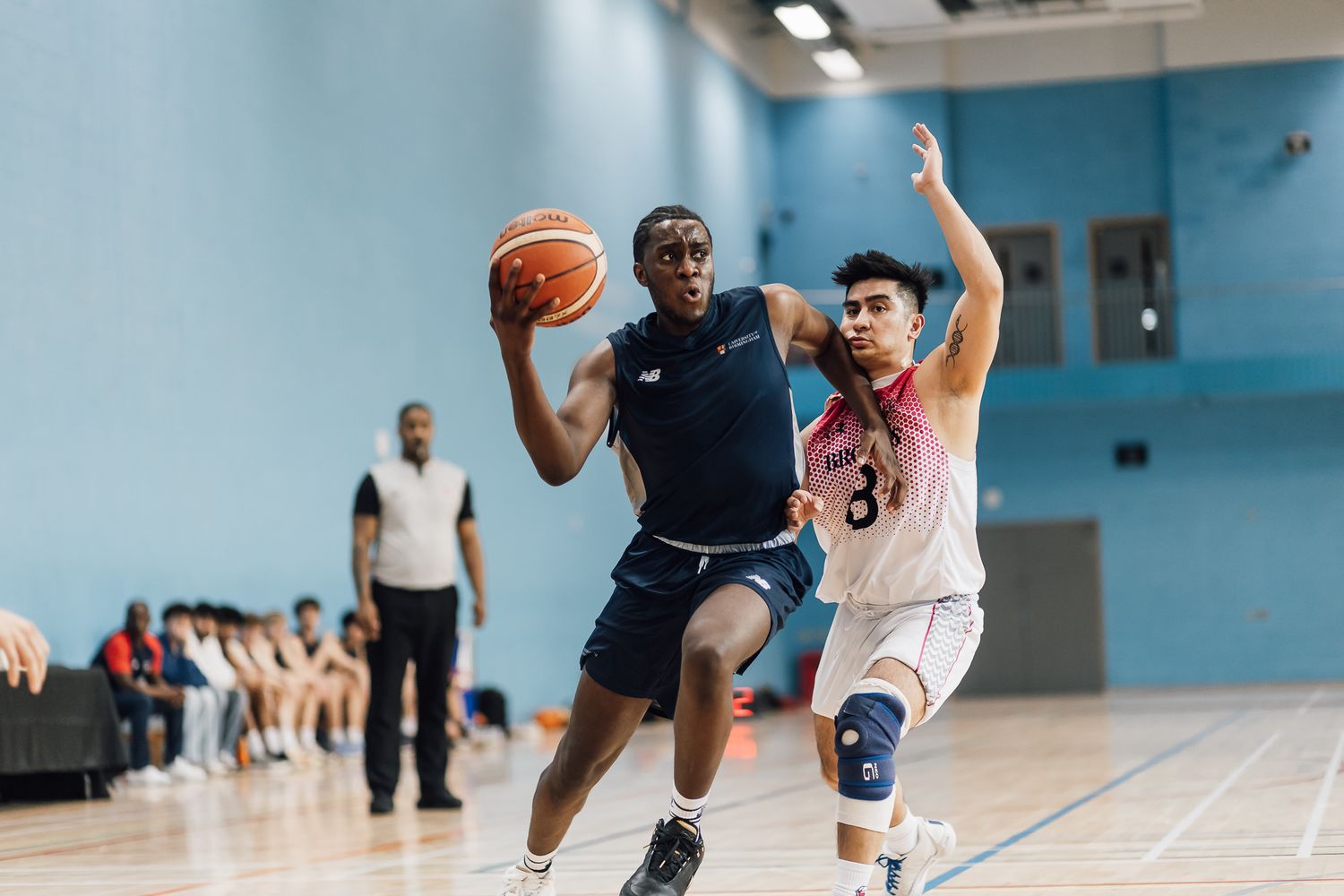 Players drive to the basket during competitive basketball game on indoor court.